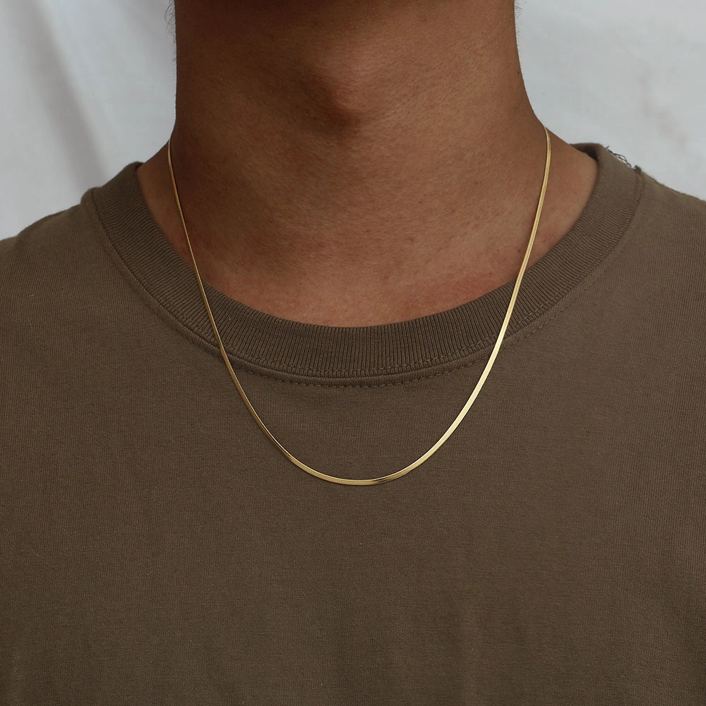 Gold necklace worn by a person wearing a brown shirt against a white background