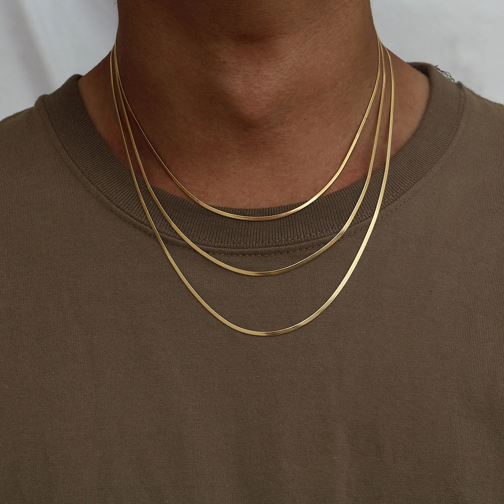 Person wearing a gold necklace on a plain background, showing different chain lengths
