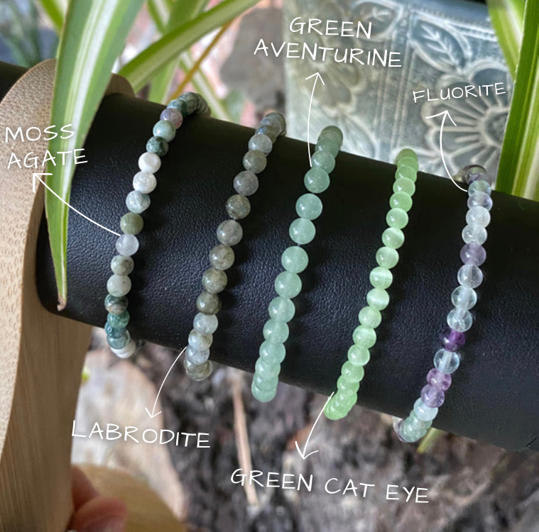 a display stand showing three different stacking stretch bracelets made with 4mm Moss Agate, labrodite, green cat eye, green aventurine and fluorite.