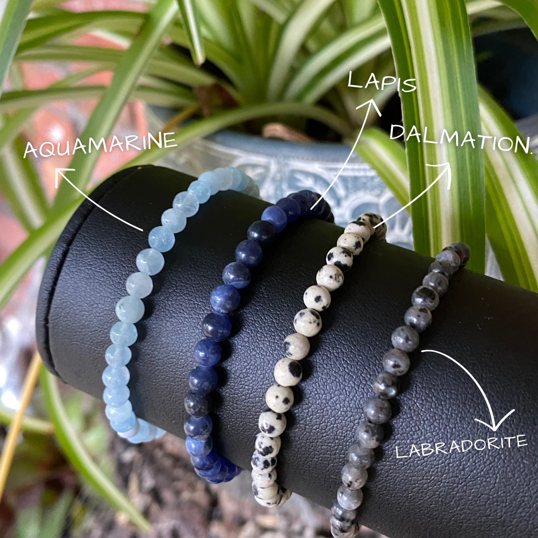 a display stand showing three different stacking stretch bracelets made with 4mm Aquamarine, lapis lazuli, Dalmatian stone and black labradorite.
