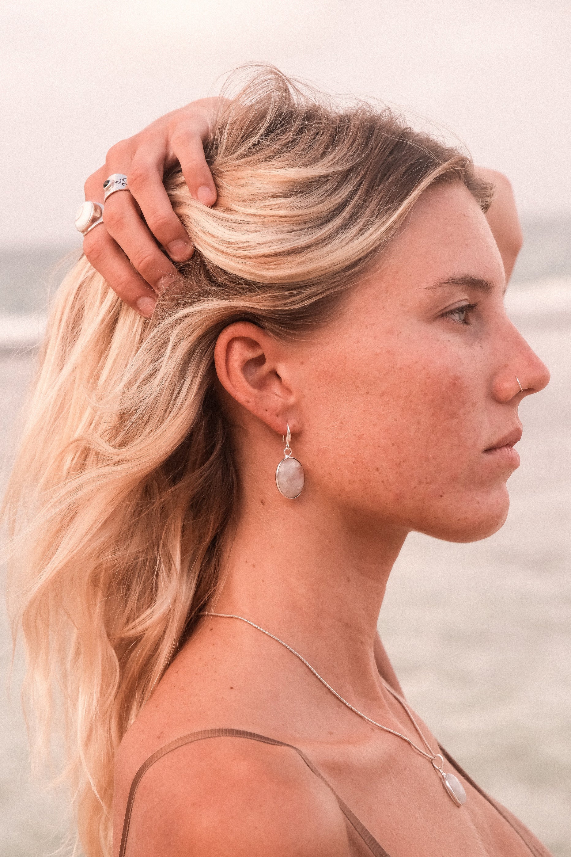 This image highlights a stylish and elegant earring, featured on the ear of a woman. The earring is sophisticated, featuring a small, possibly semi-precious stone, attached to a delicate chain that extends to a sleek, metallic loop.