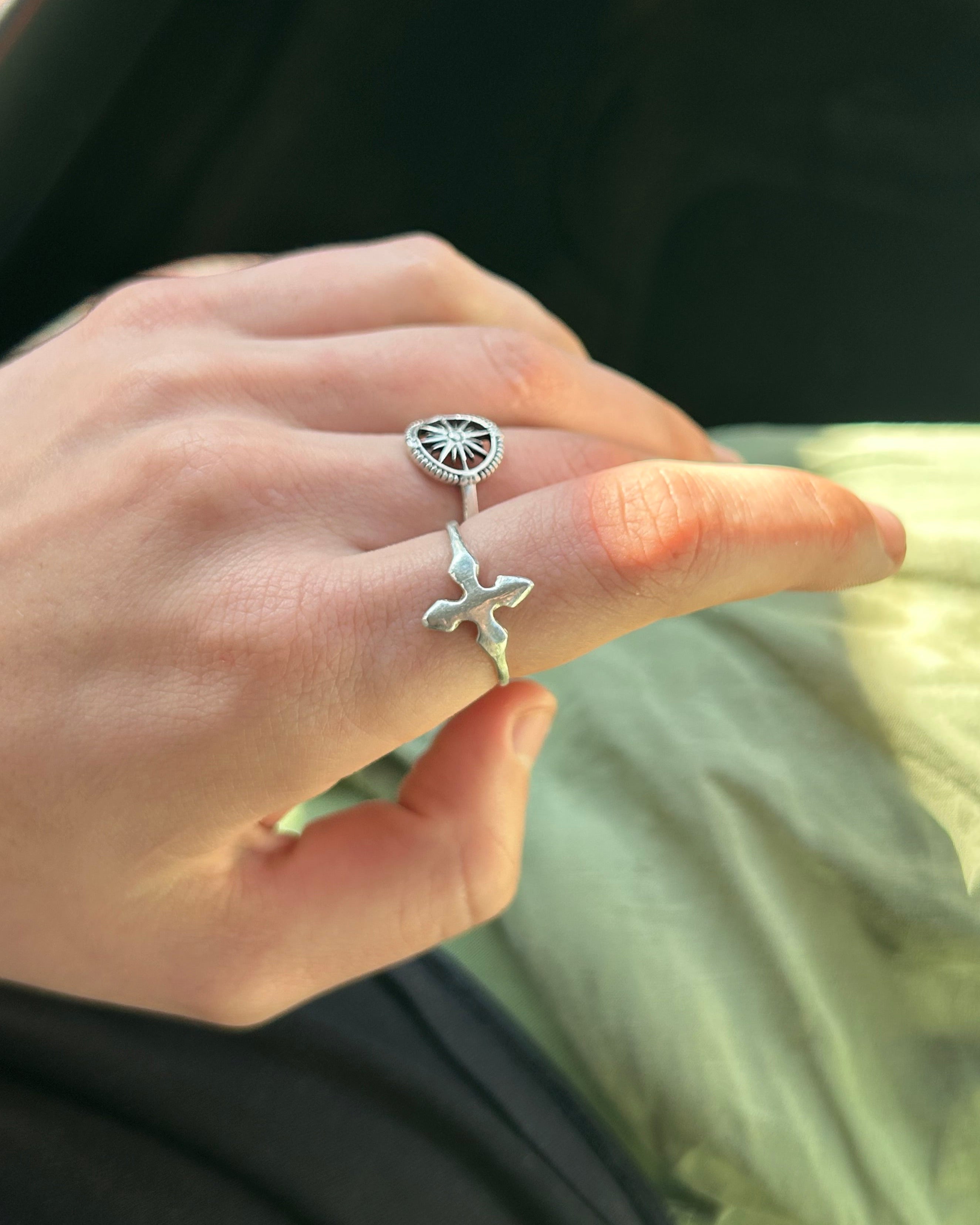 Hand wearing two silver rings with intricate designs against a blurred background