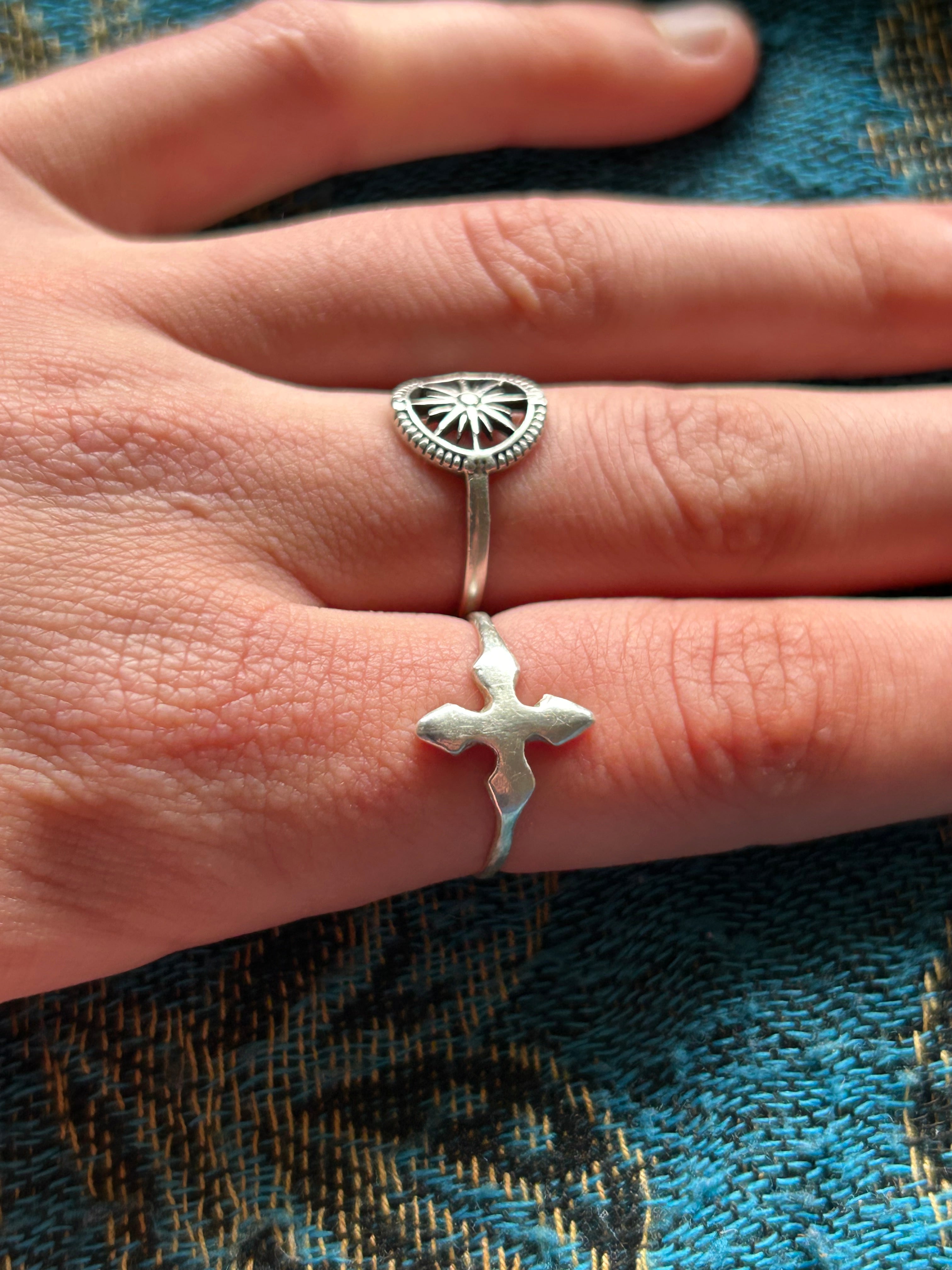 Hand wearing two silver rings with a detailed design on a textured fabric background