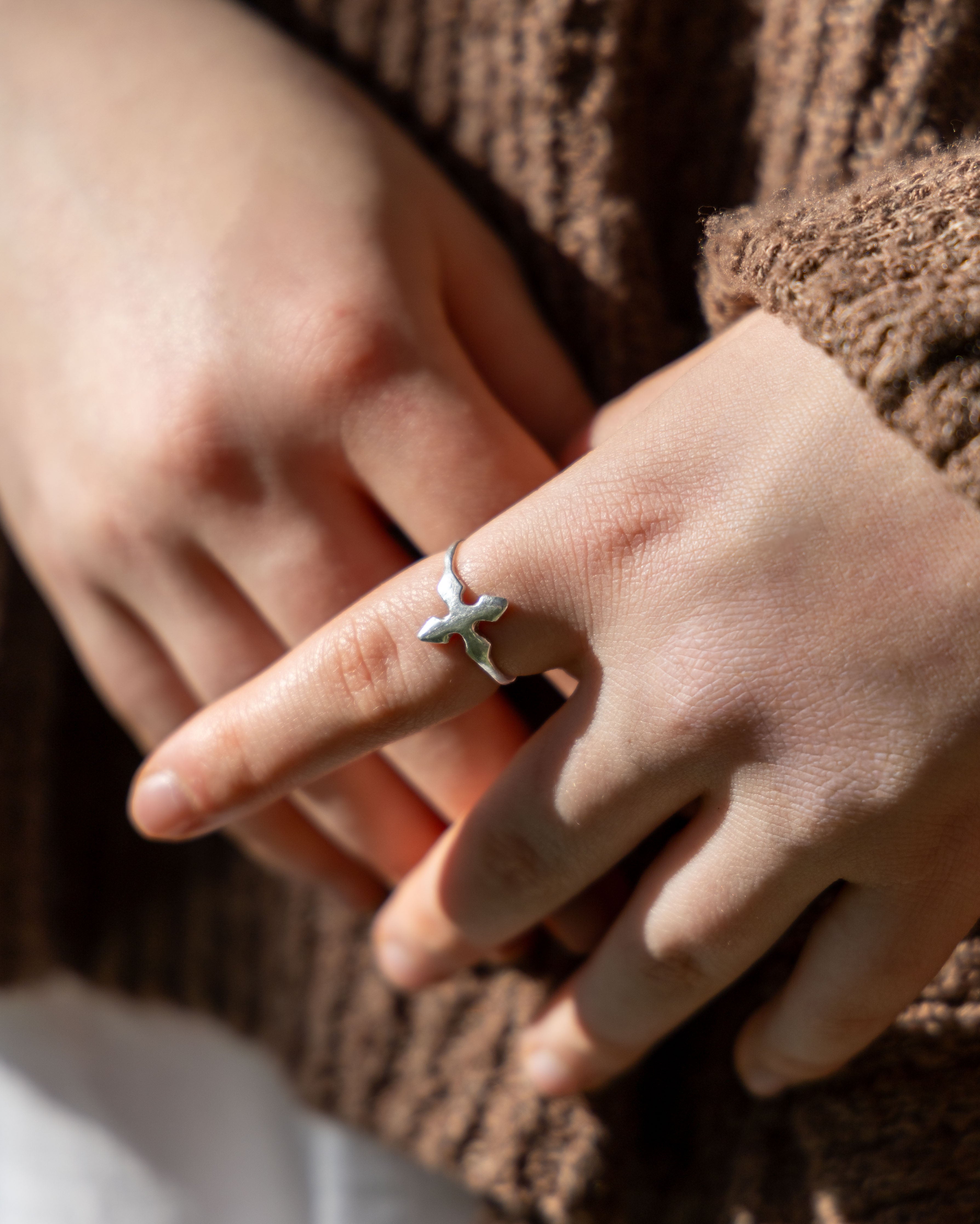 Hand wearing a silver ring with a bird design on a brown textured fabric background