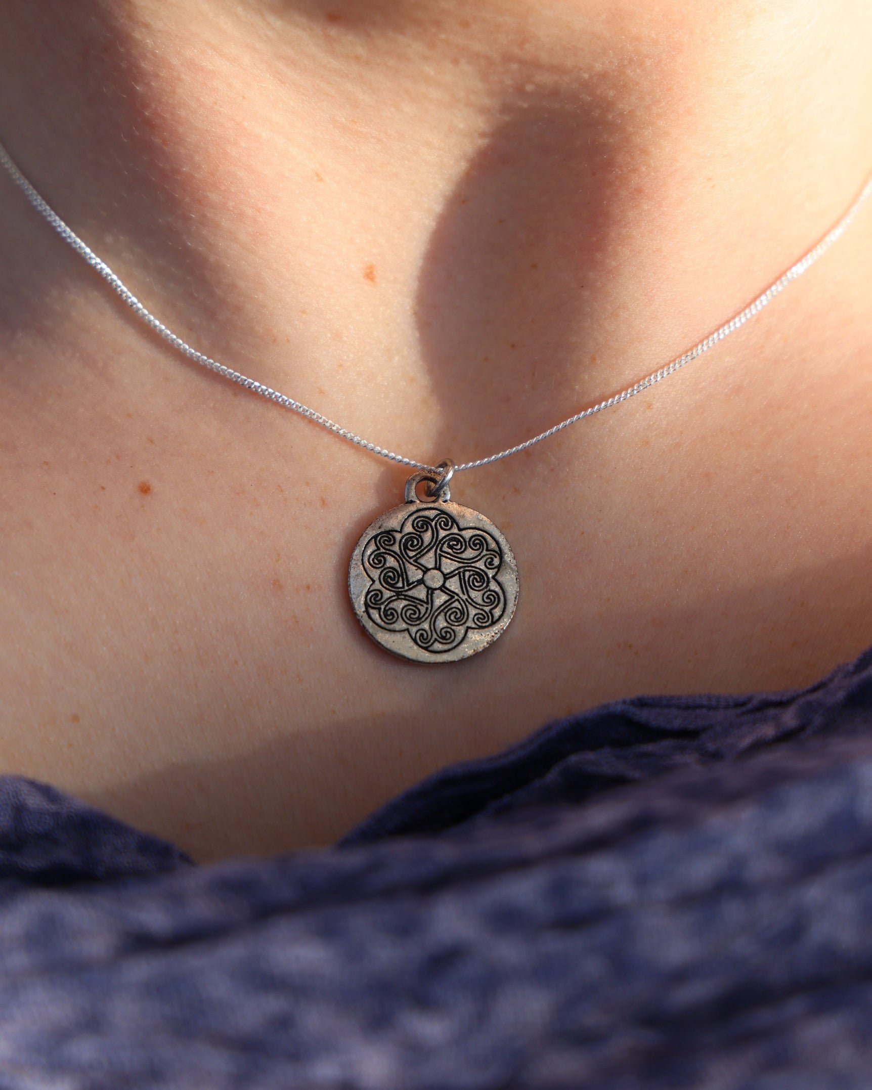 Close-up of a silver necklace with a floral pendant on a person's neck.