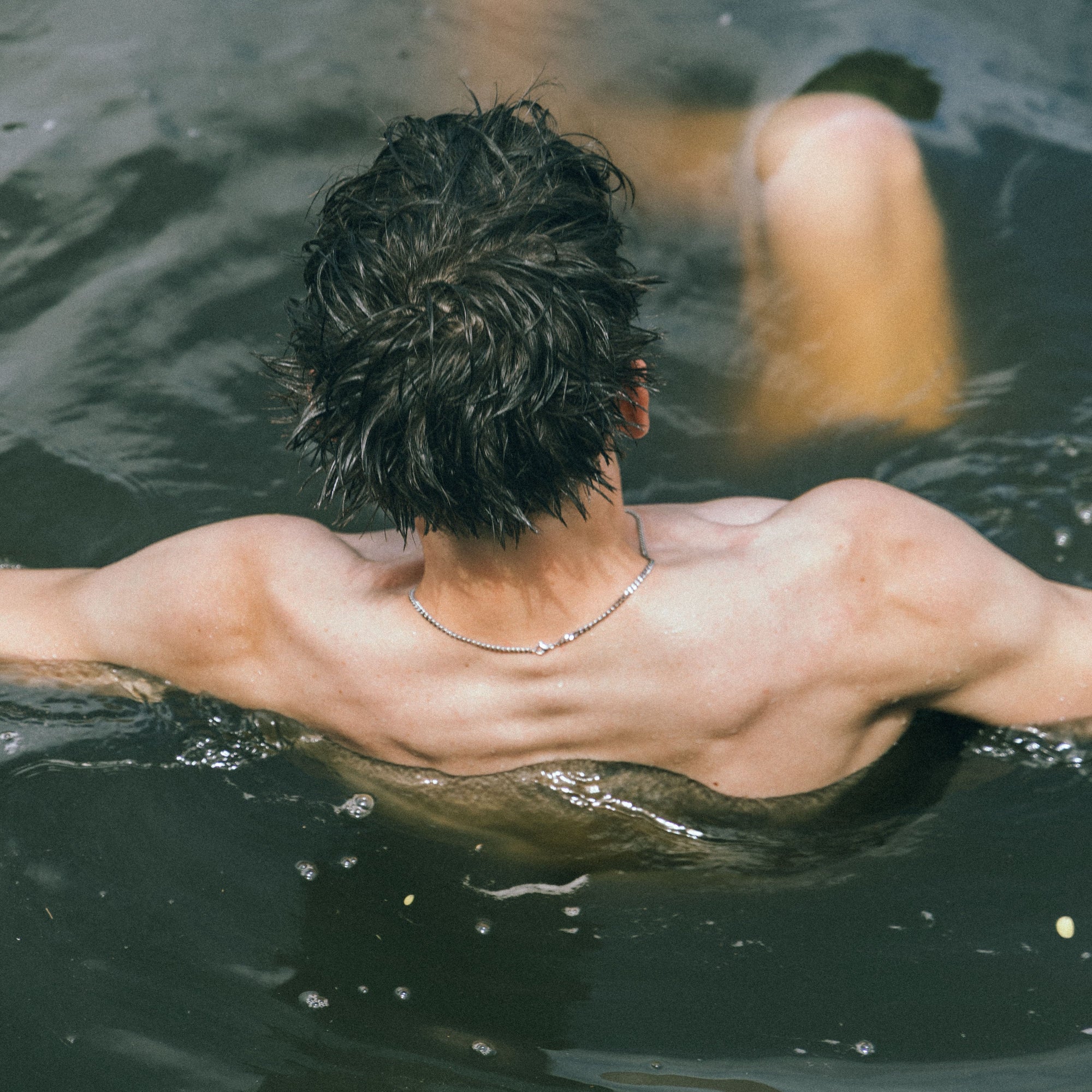 Person diving into water wearing necklace with a blurred background