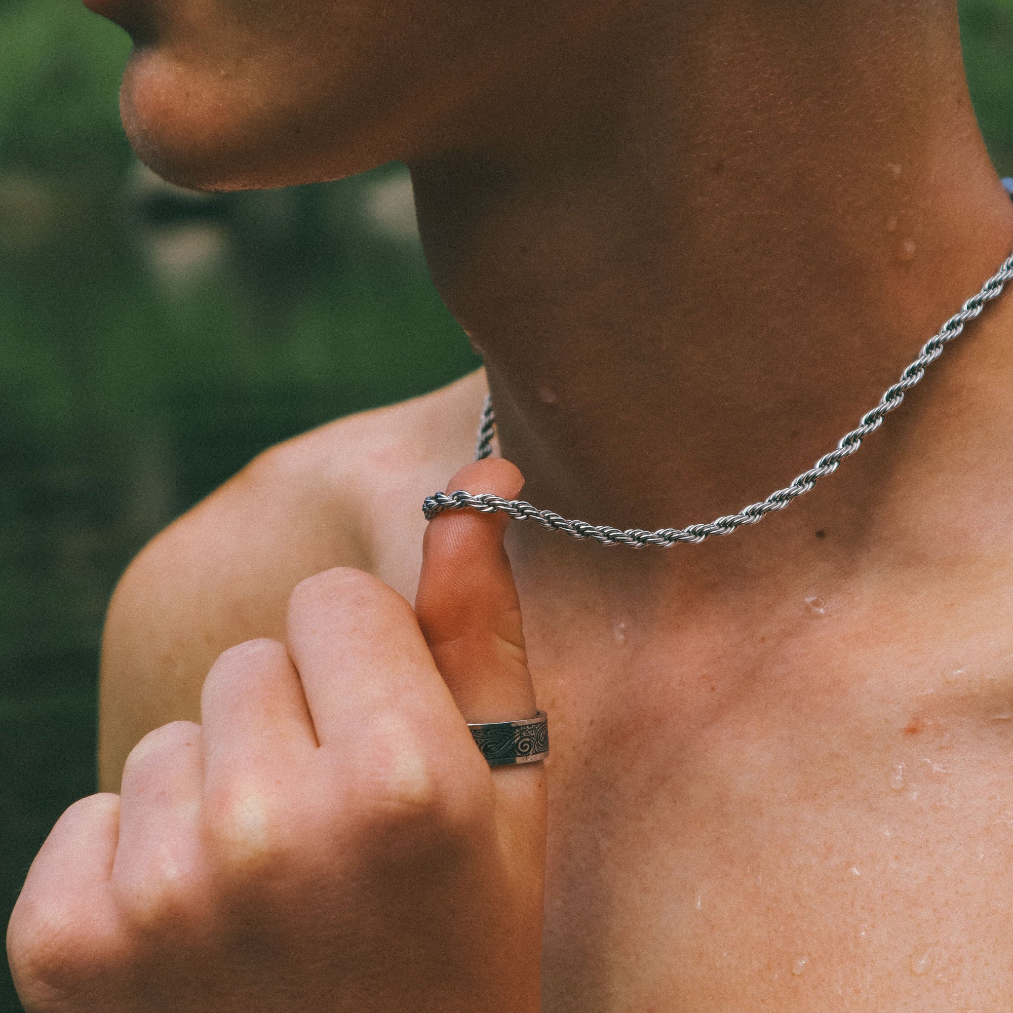Close-up of a person's hand with a ring on a chain, against a blurred natural background.