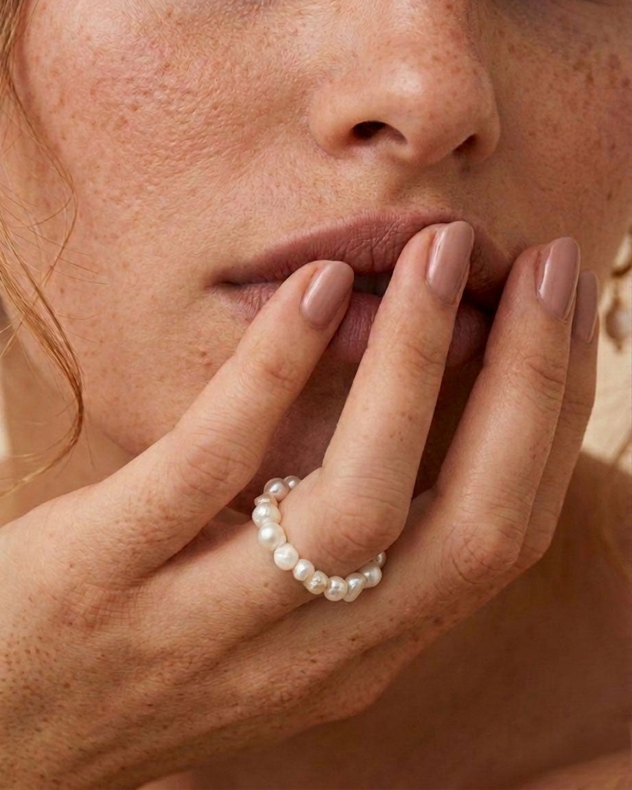 Close-up of a woman's hand with a pearl ring on her finger, touching her lips.