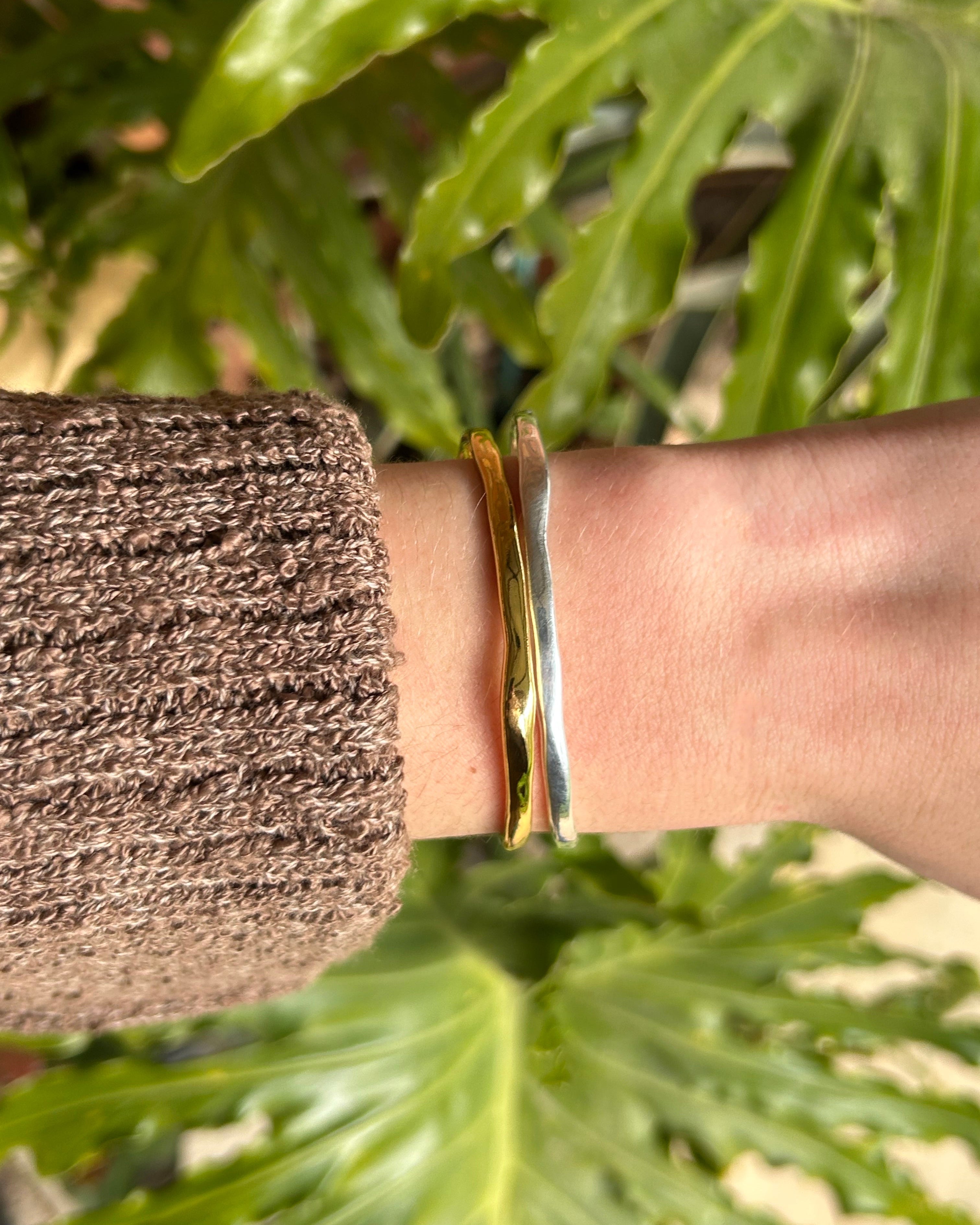 Gold and silver bracelet on a wrist with a blurred green leafy background