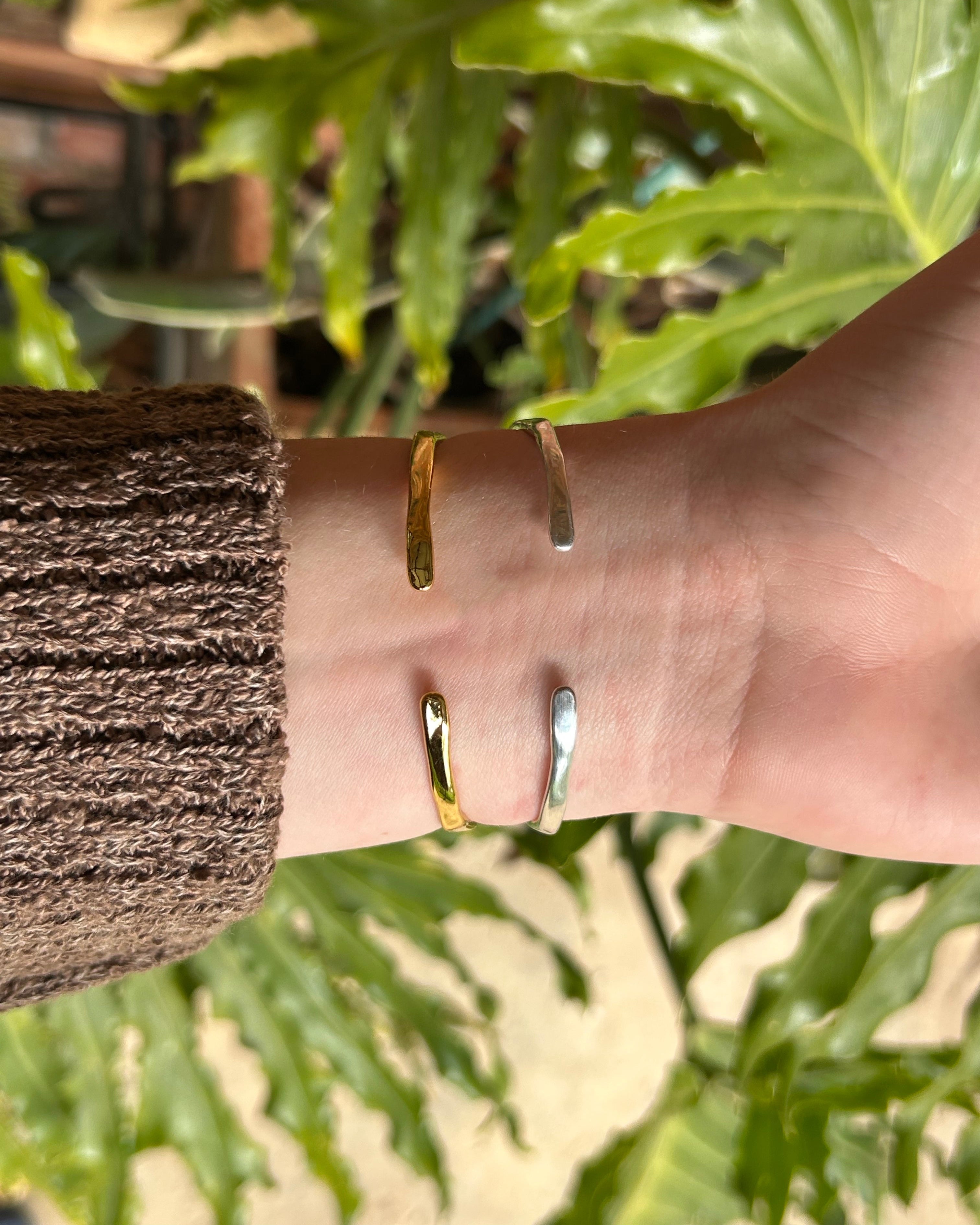 back of adjustable Gold and silver cuff on a wrist with a blurred green leafy background
