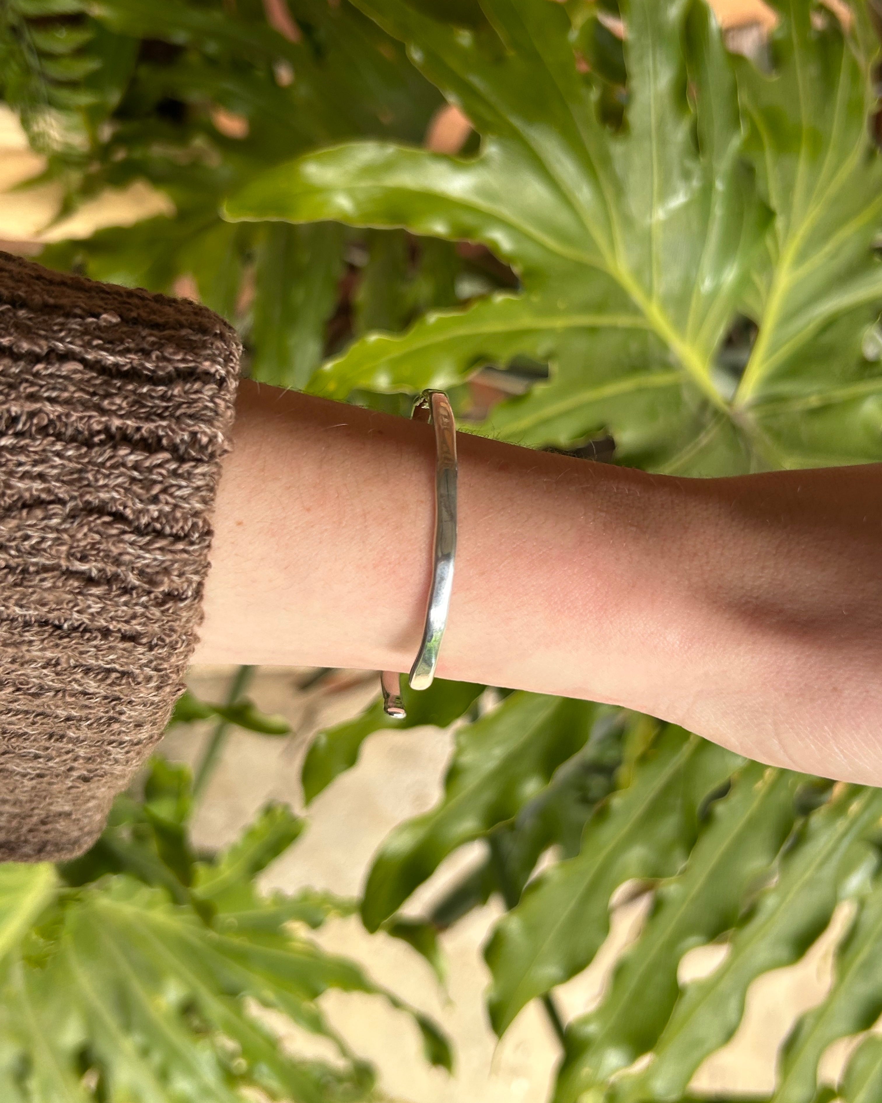 Silver bracelet on a wrist with a blurred green leafy background