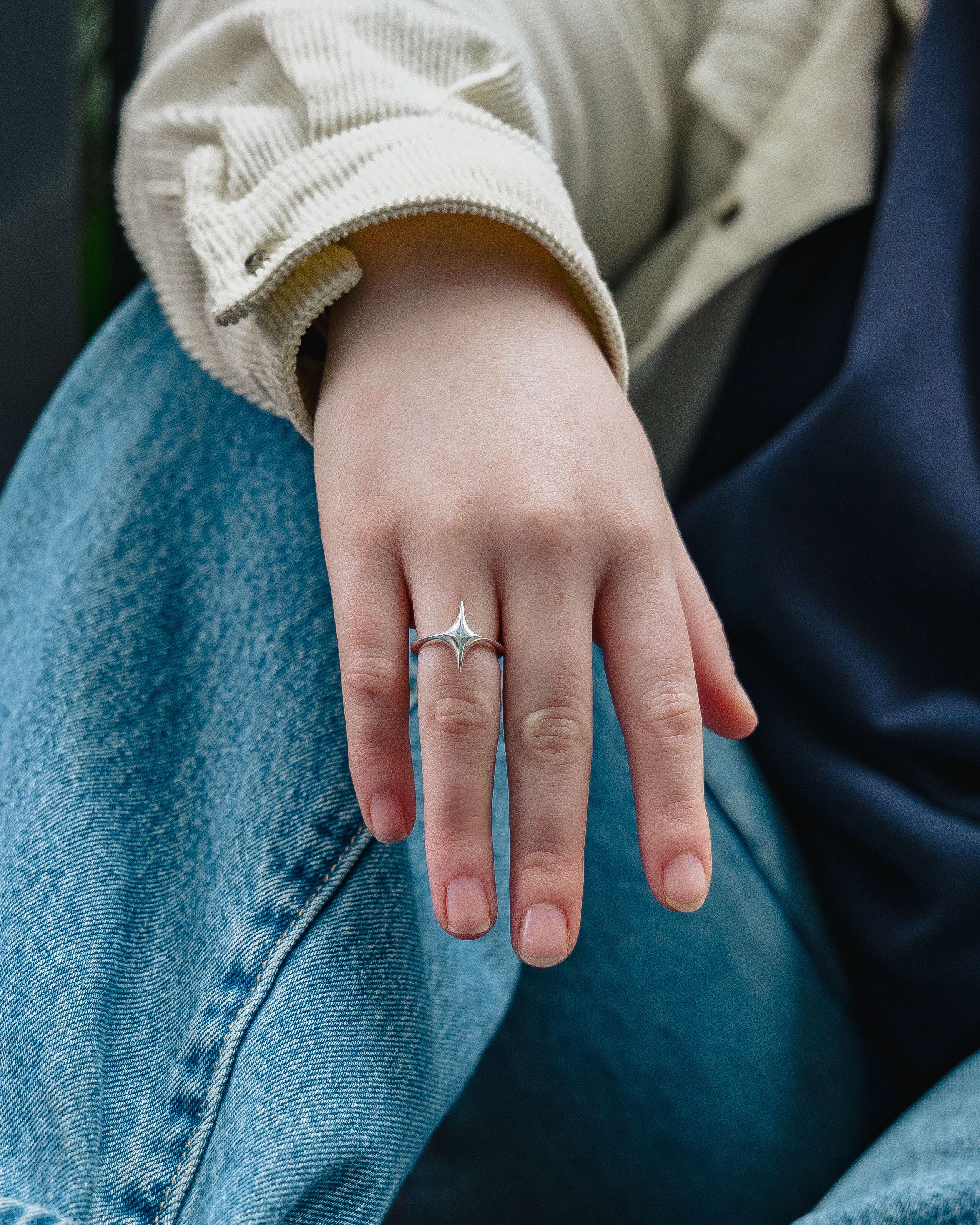 Hand wearing a silver star shaped ring on a blue denim background