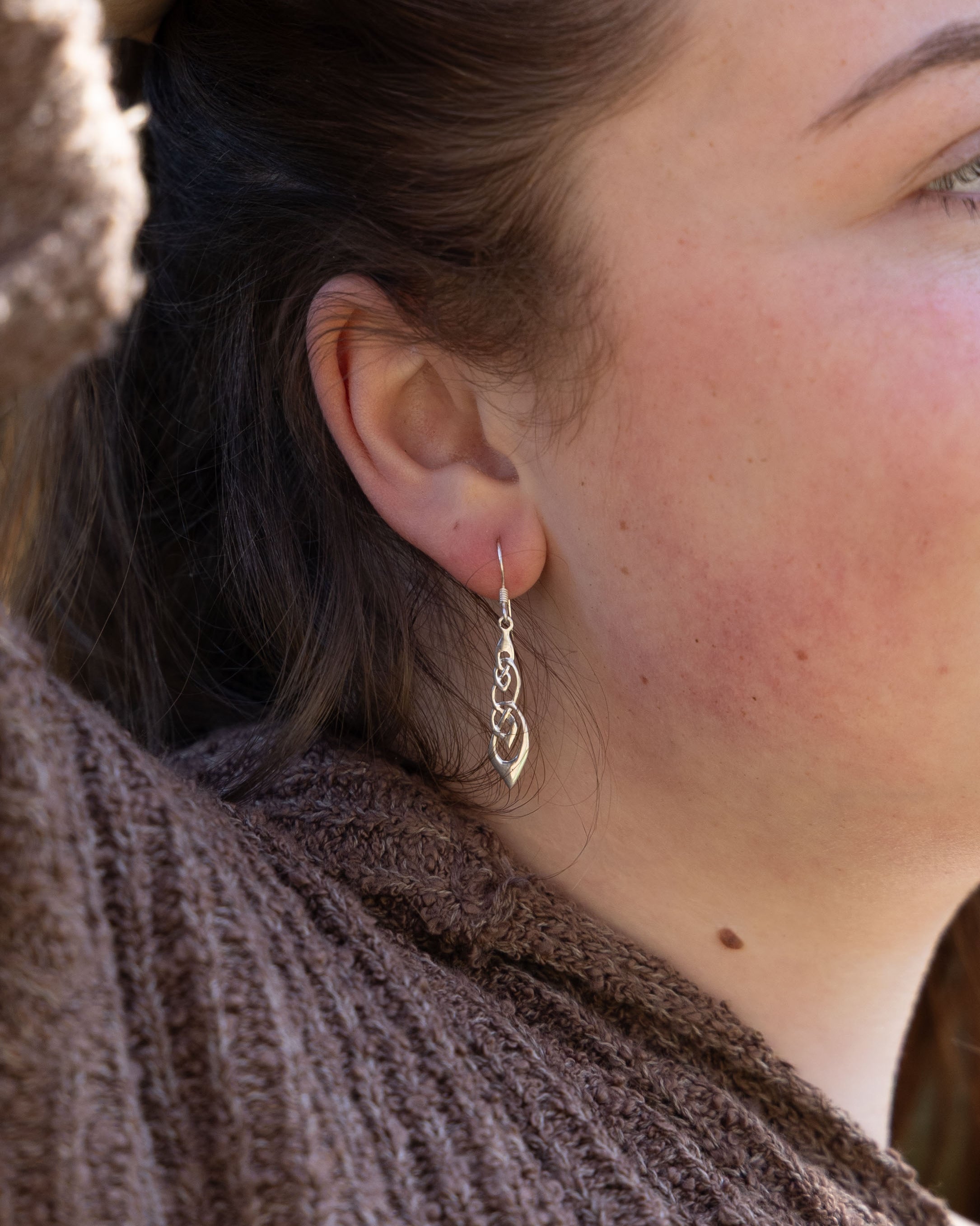 Close-up of an ear with a silver earring, wearing a brown textured garment.
