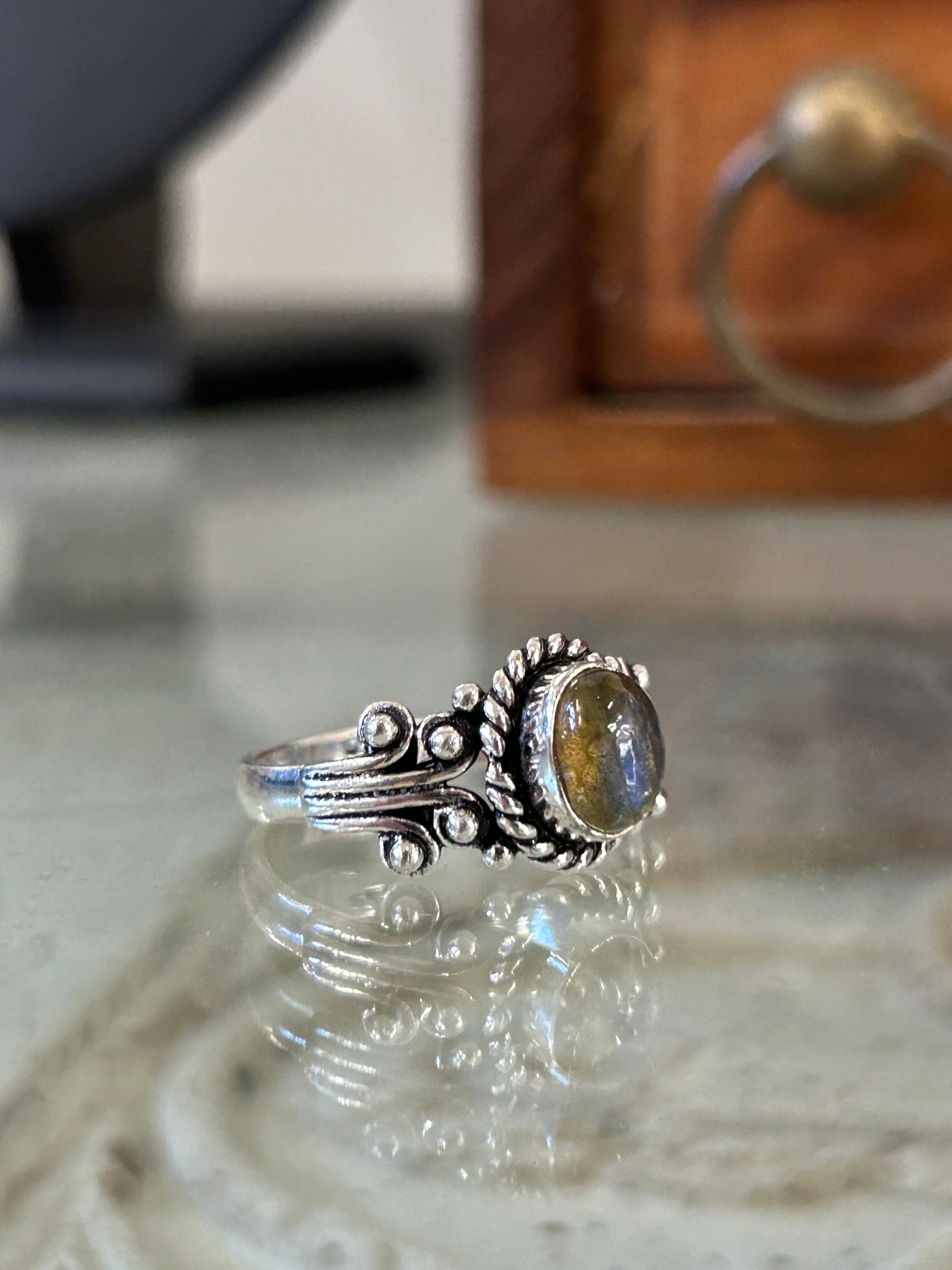 A silver ring with a labradorite stone, featuring intricate detailing on a reflective surface.