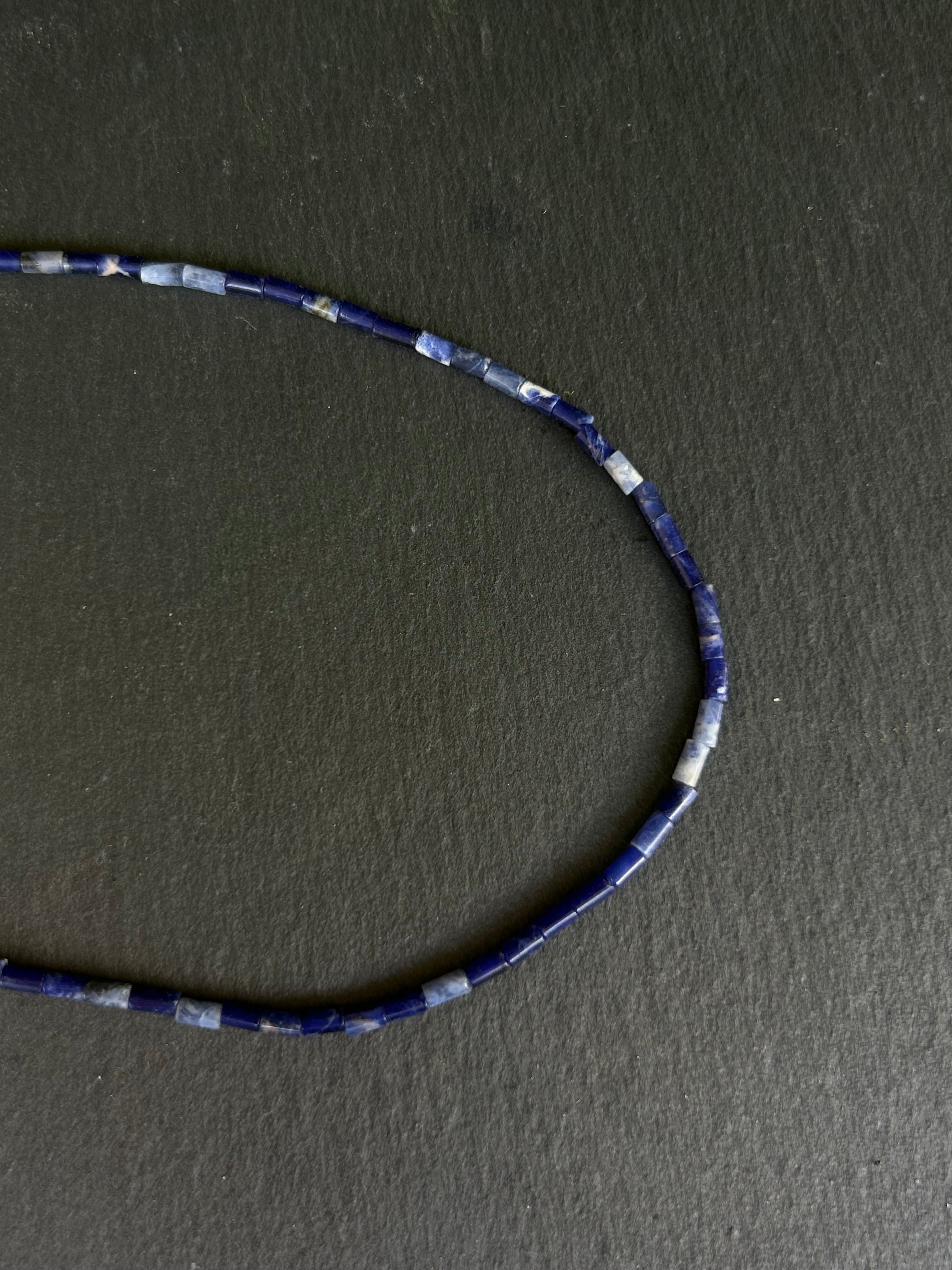 A Lazuli lapis beaded necklace with a variety of earthy tones, laid out on a dark background.