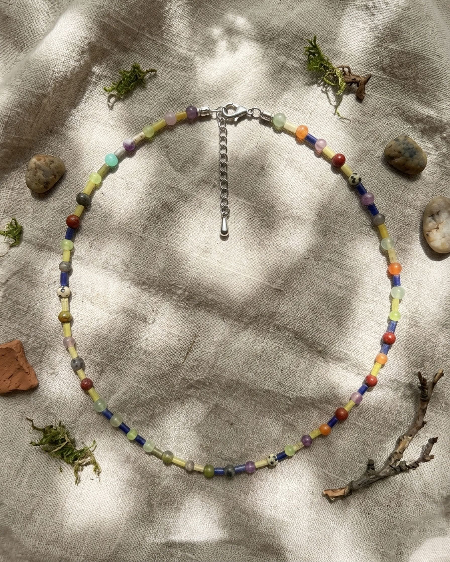Colorful beaded necklace on a textured fabric background with natural elements.