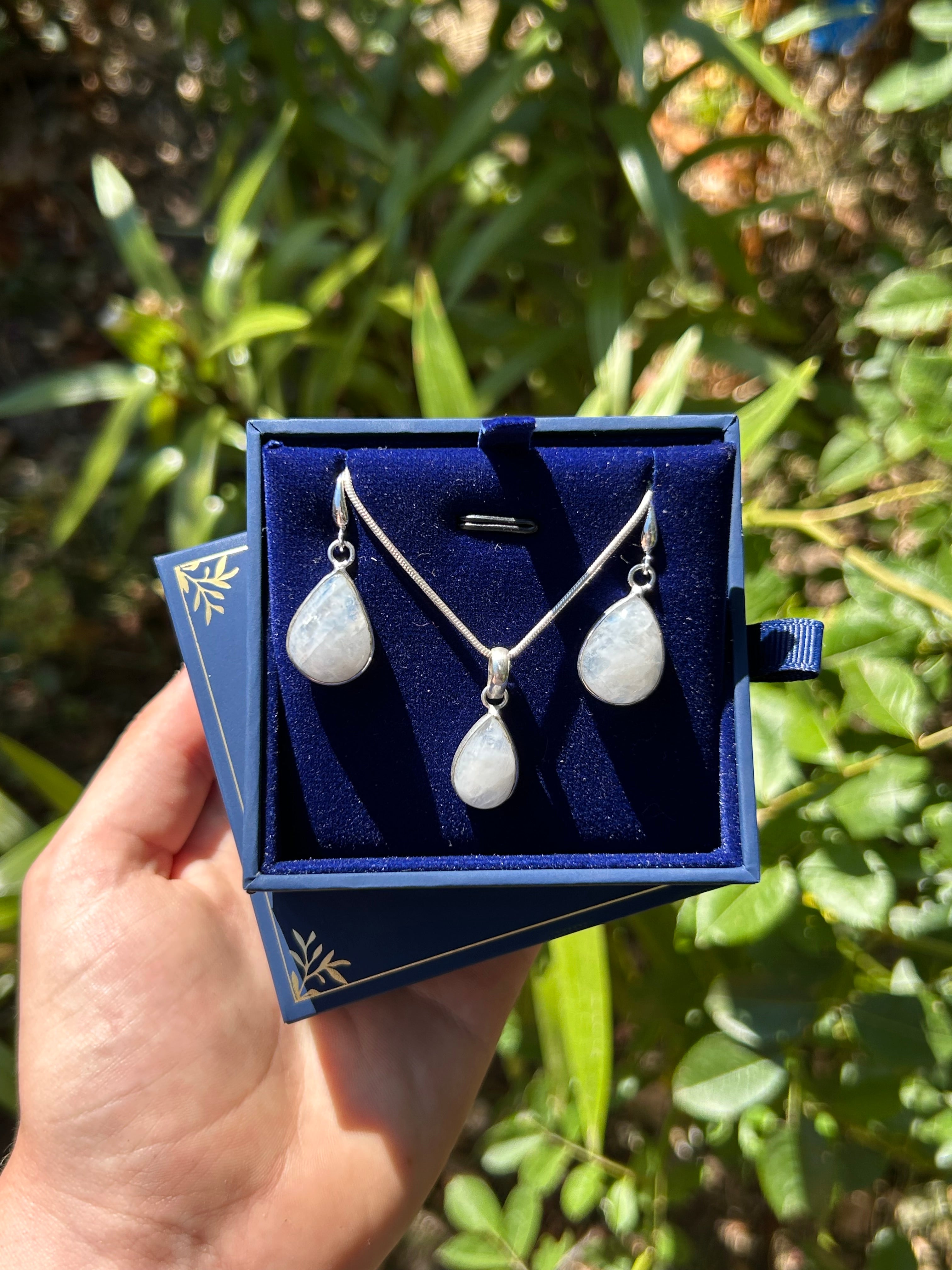 Jewelry set with teardrop-shaped stones in a blue box held by a hand against a green leafy background