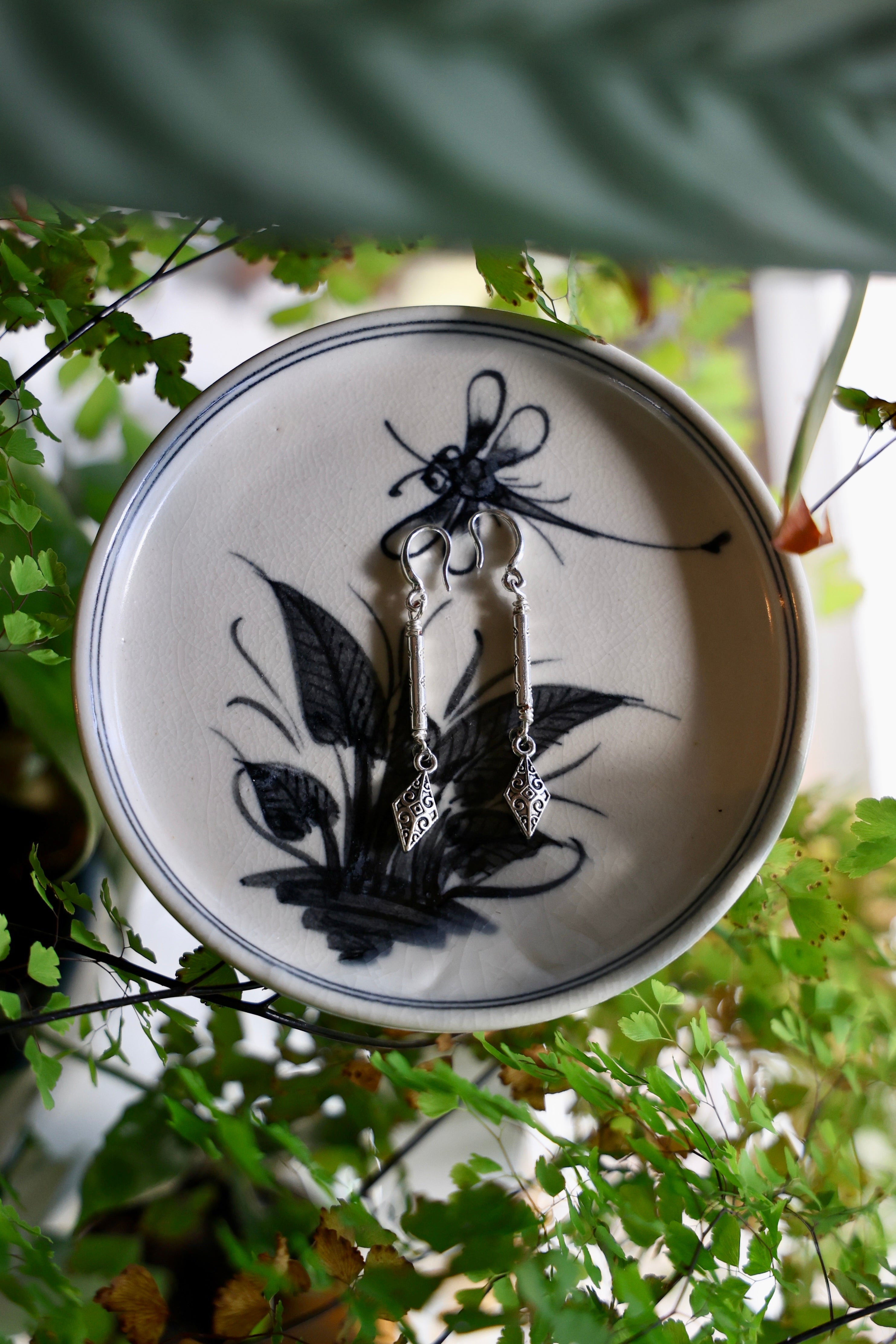 Pair of earrings on a decorative plate with floral design, surrounded by green foliage.
