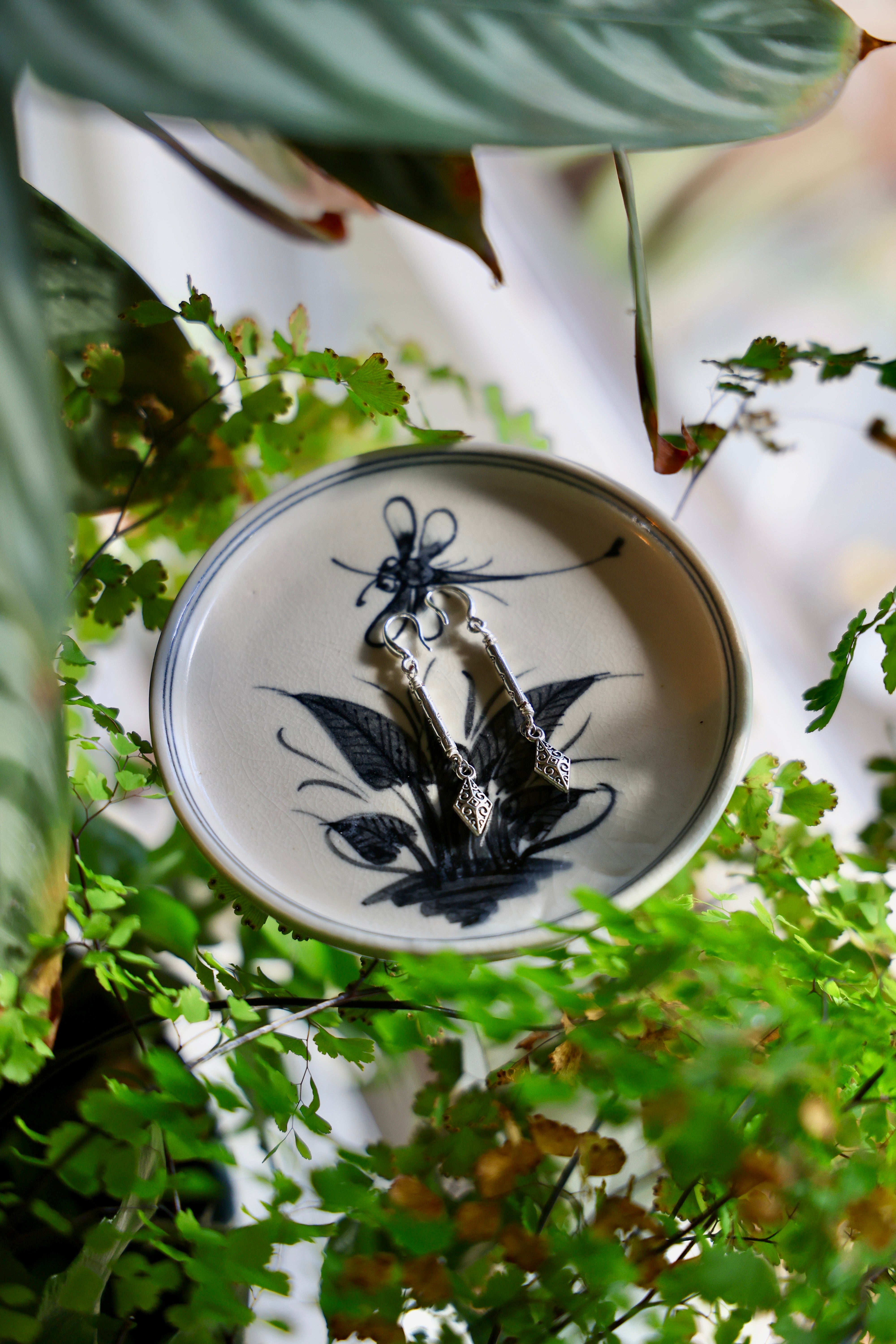 Decorative plate with black floral design on a white background, surrounded by green foliage.