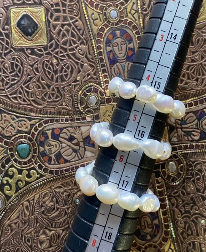A ring with freshwater pearls displayed on a measuring scale, with decorative items in the background.