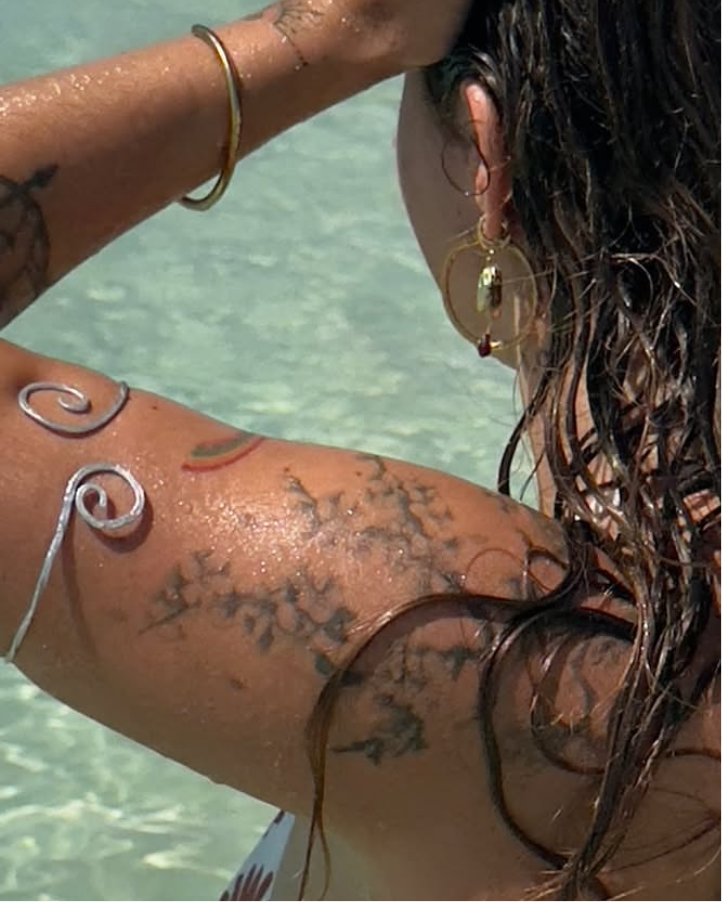 Person with tattoos and jewellery by a body of water. wearing the adjustable upper arm bracelet in silver, showcasing how the boho wire arm cuff fits on the bicep.