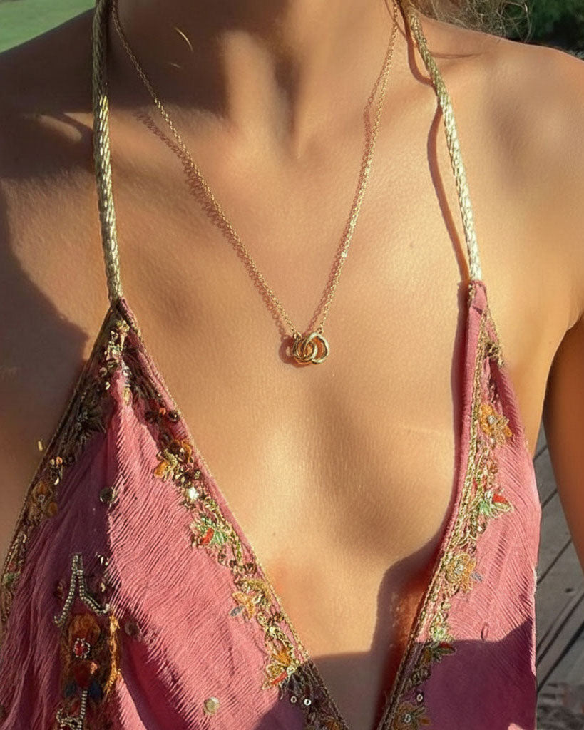 Close-up of a person wearing a pink embroidered top with interlocked organic rings necklace