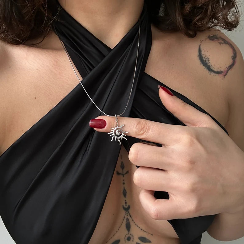 Person wearing a black top with a sun pendant necklace, highlighting the necklace.