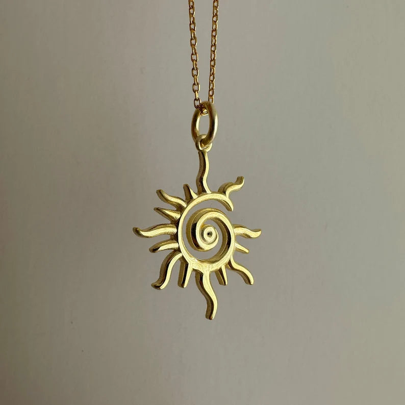 Gold sun-shaped pendant on a chain against a neutral background