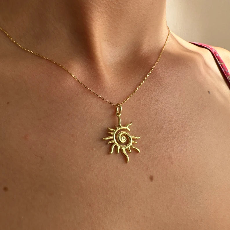Gold sun-shaped pendant necklace on a person's neck with a neutral background