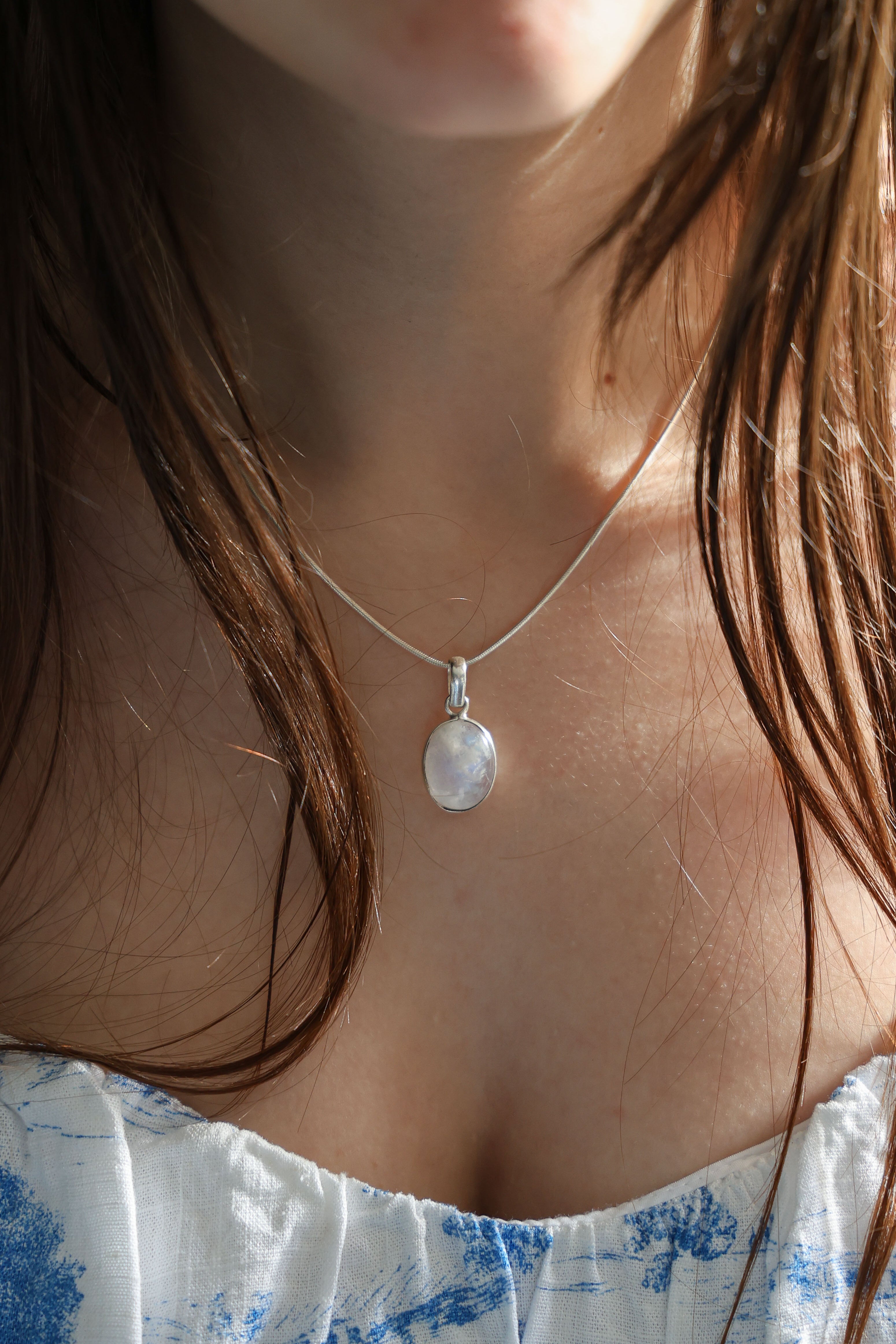 A person wearing a silver necklace with a moonstone pendant.