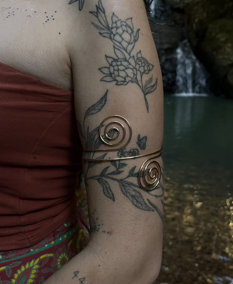 model is wearing a gold spiral arm cuff with floral tattoos on the arm.