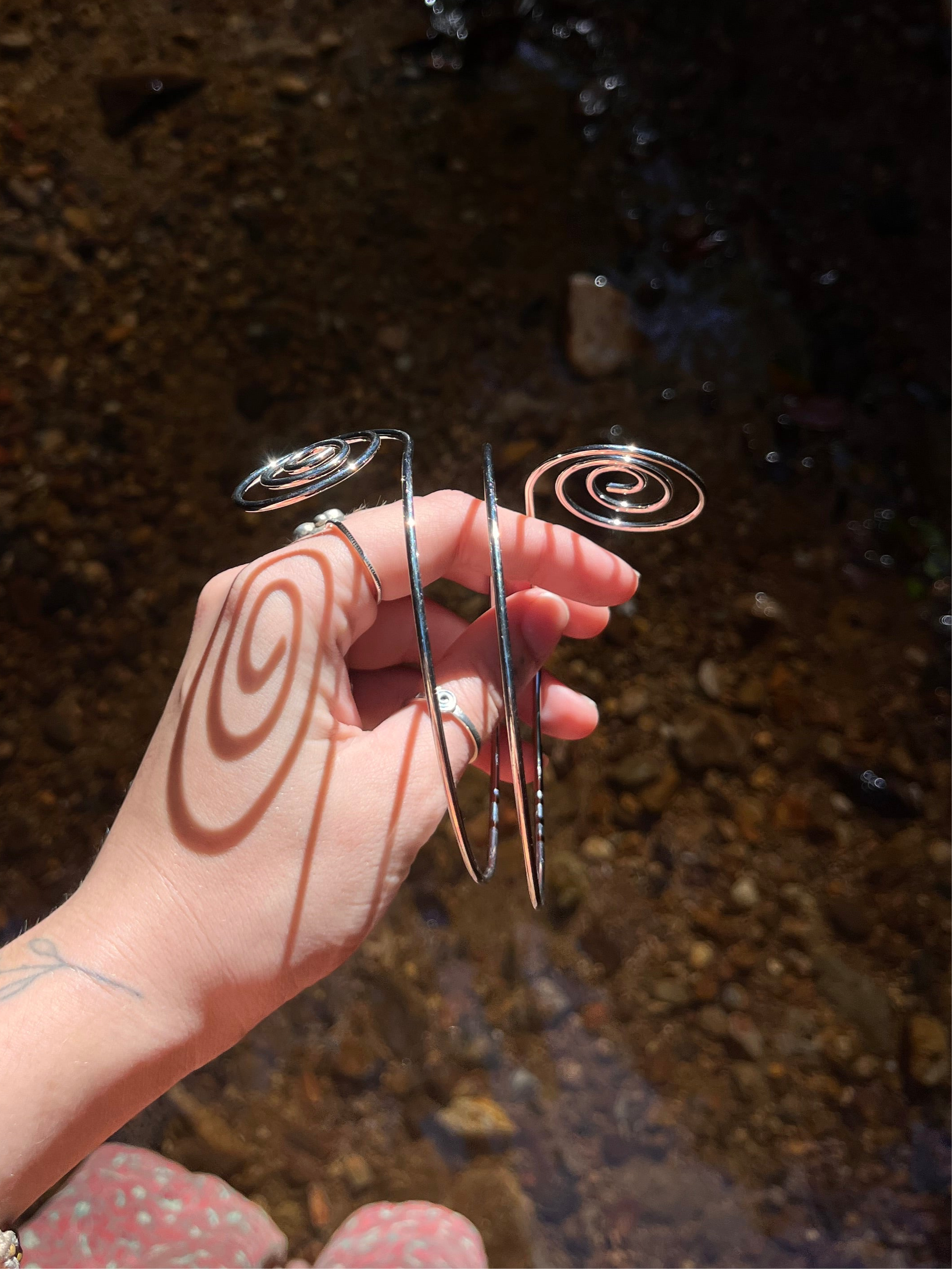 Silver spiral arm cuff held by a hand with a blurred natural background