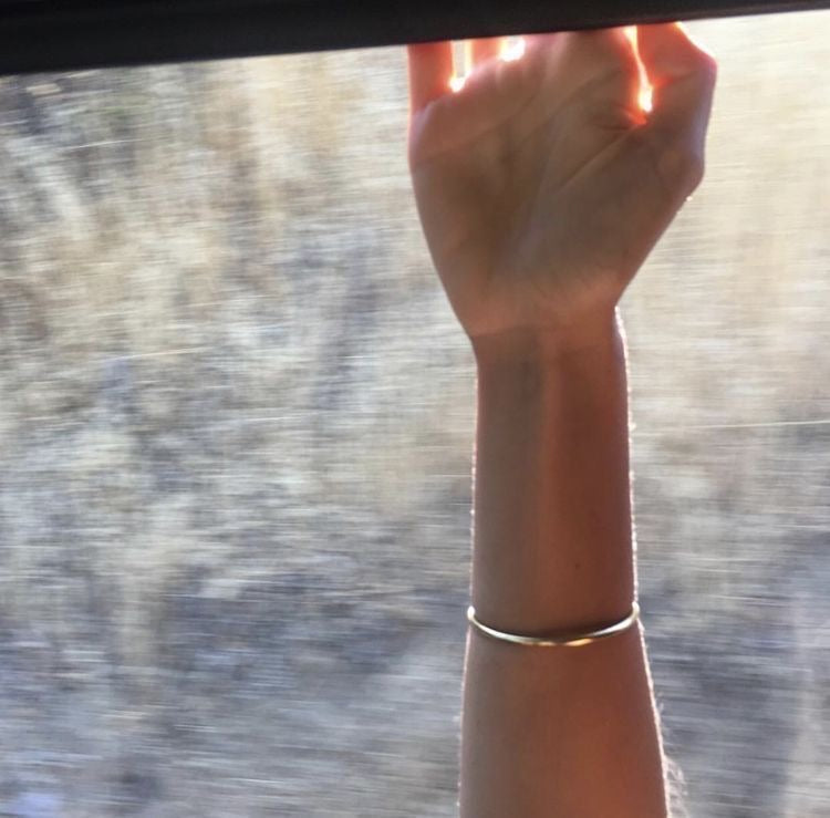 Hand with a bracelet reaching out of a window with a blurred outdoor background
