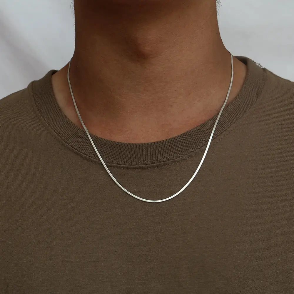 Person wearing a silver necklace against a plain background