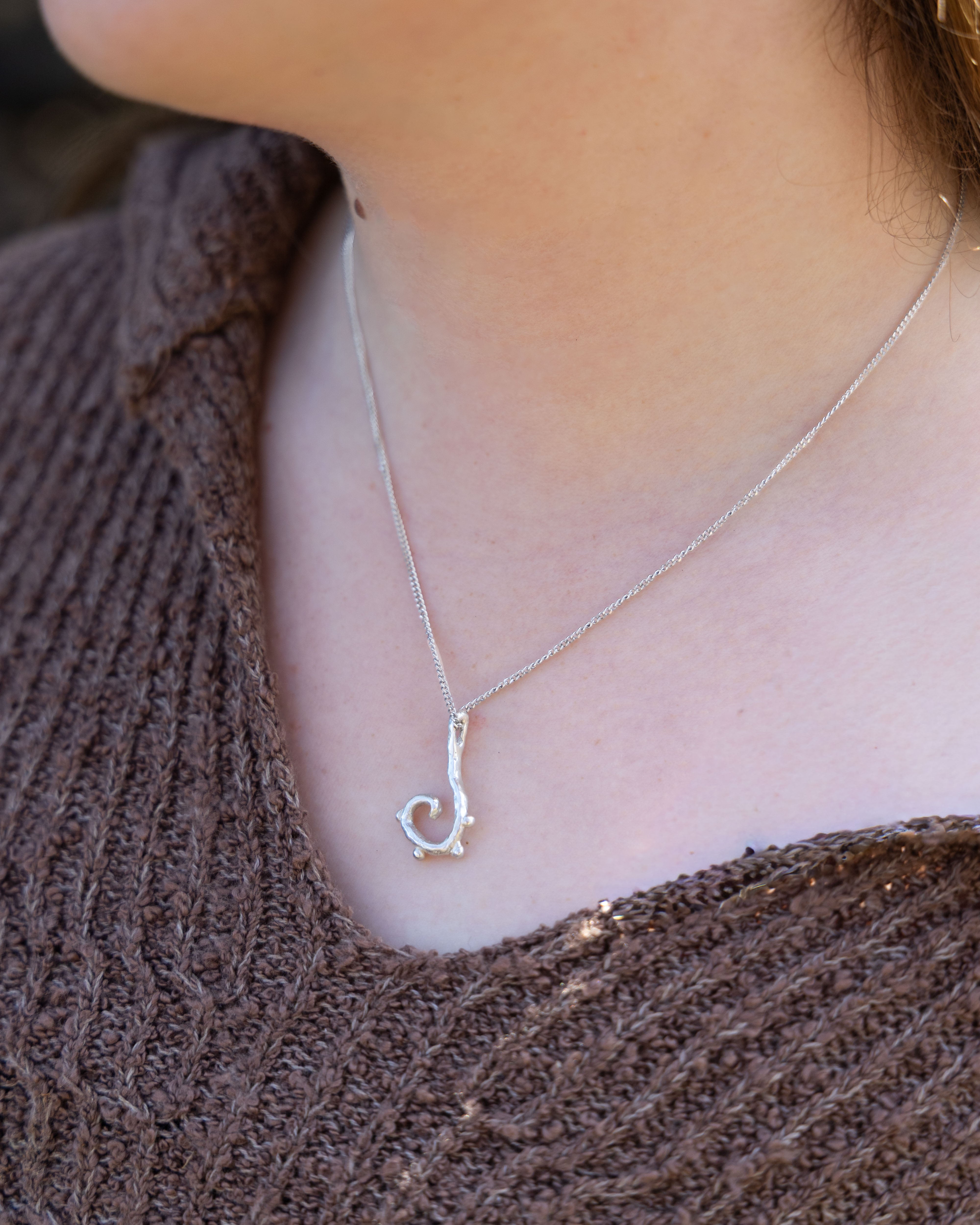 Silver necklace with a unique pendant worn by a person against a brown textured background
