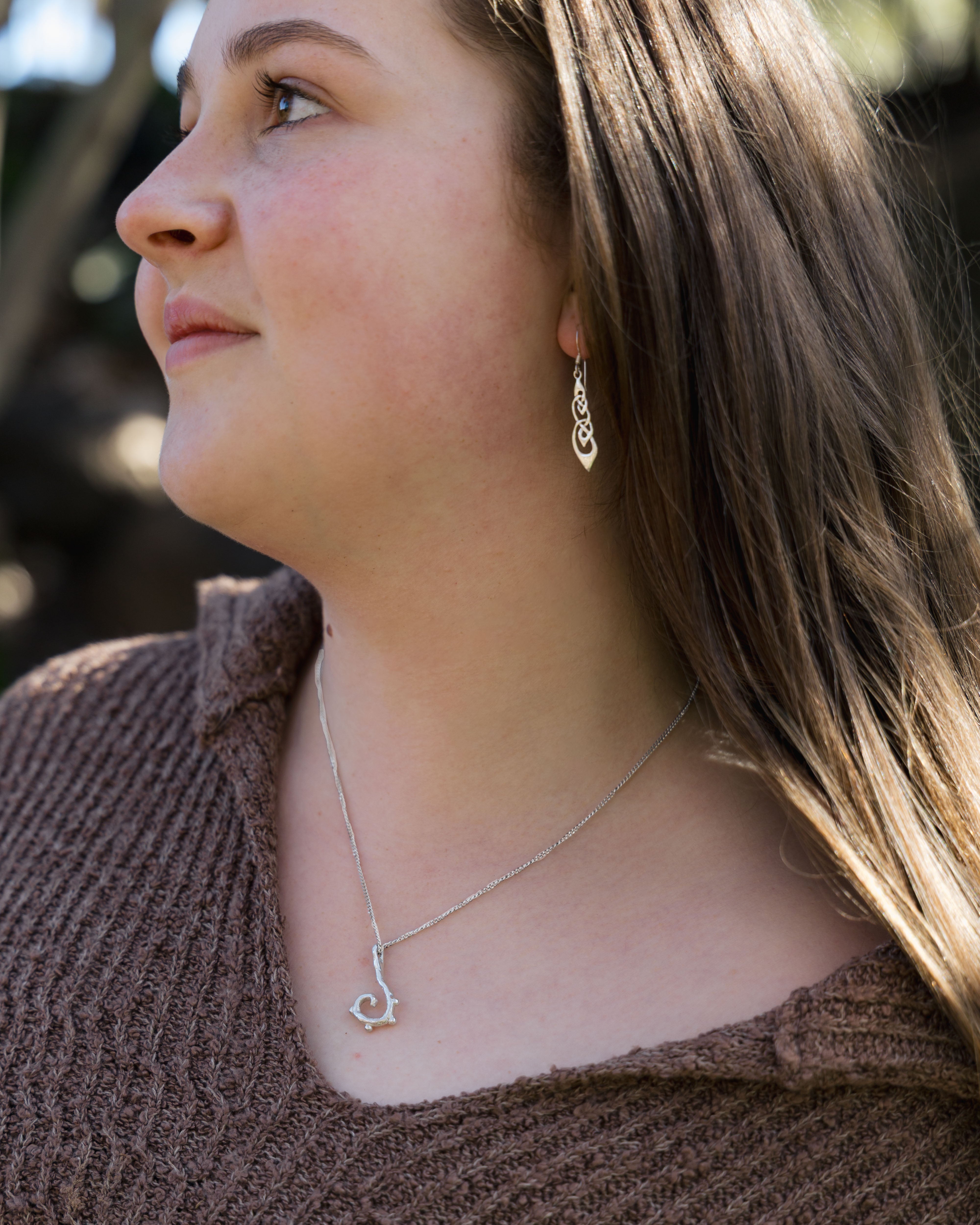 Woman wearing a delicate silver necklace with a small pendant, lying on a textured surface.