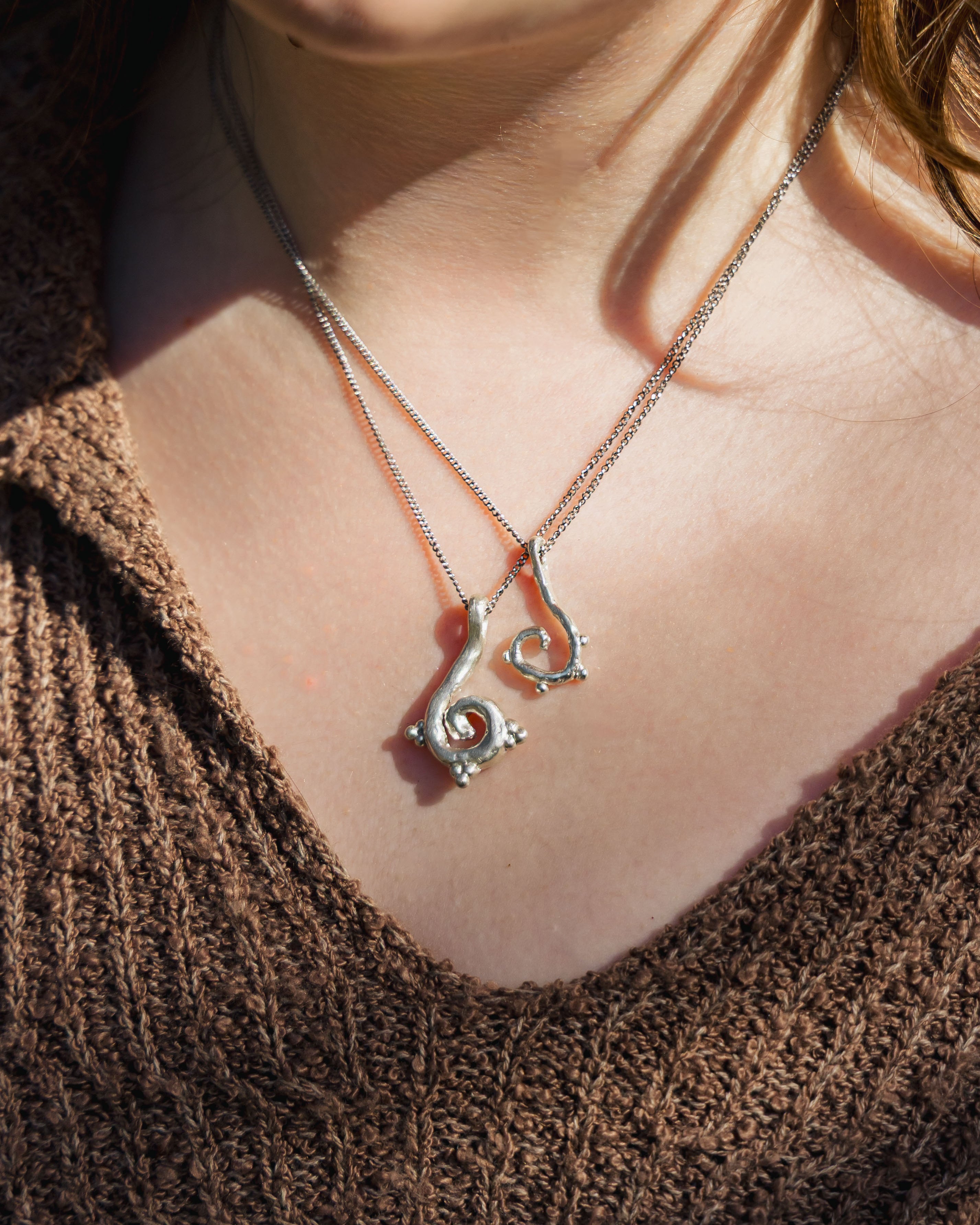 Close-up of a person wearing dainty and chunky versions on the ember necklace