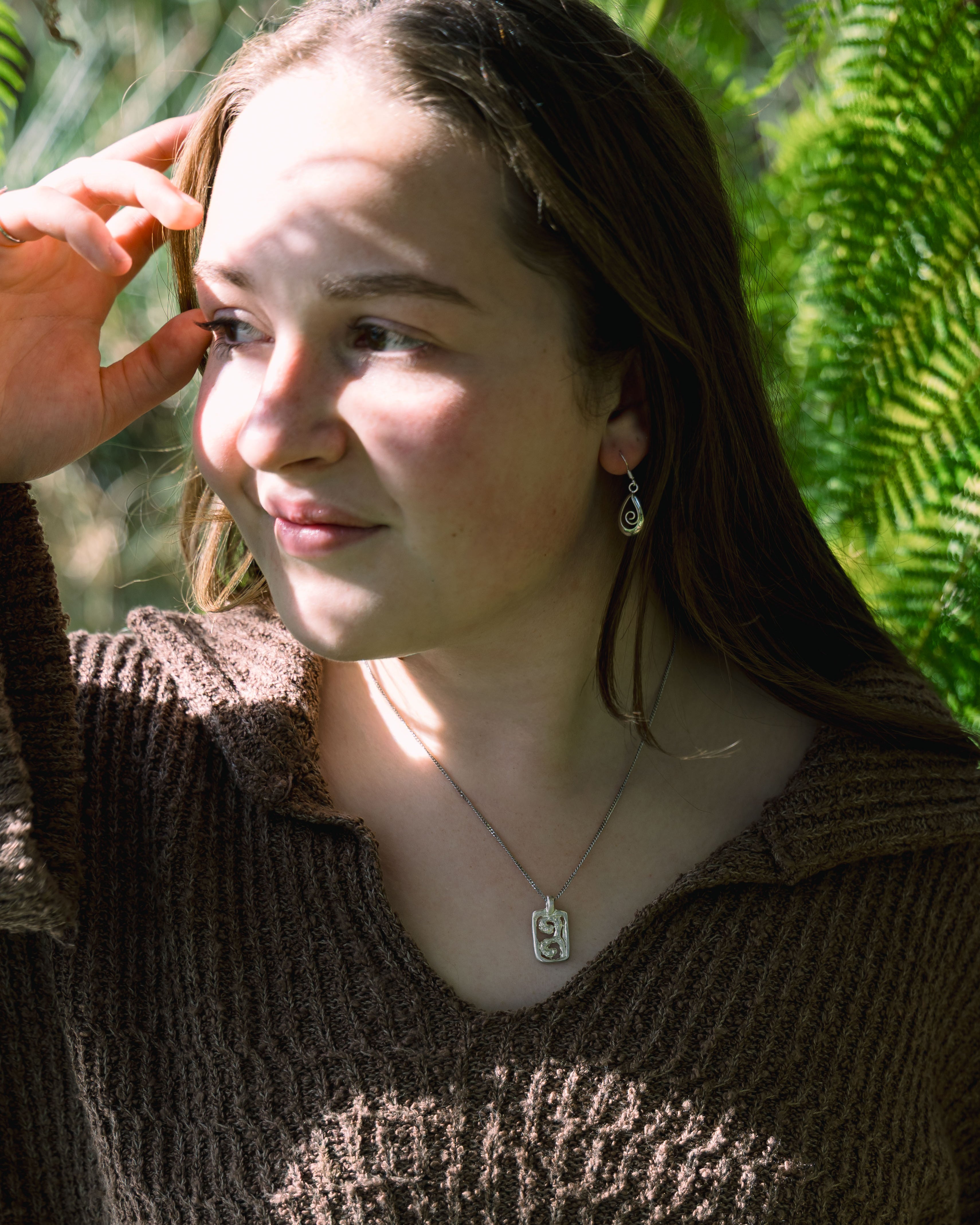 Woman with a necklace and earrings against a green leafy background