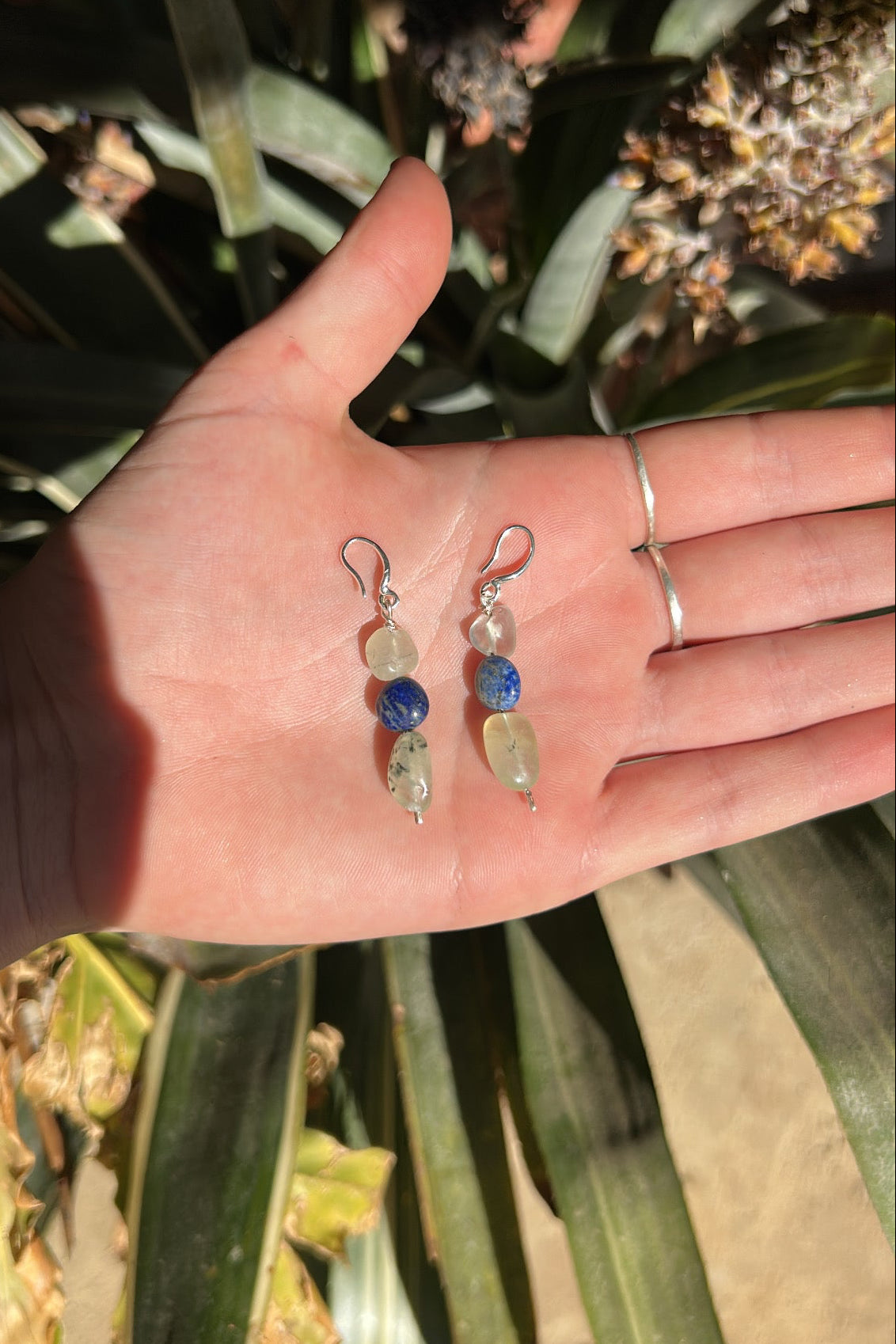 Hand holding two pairs of earrings with a blurred natural background