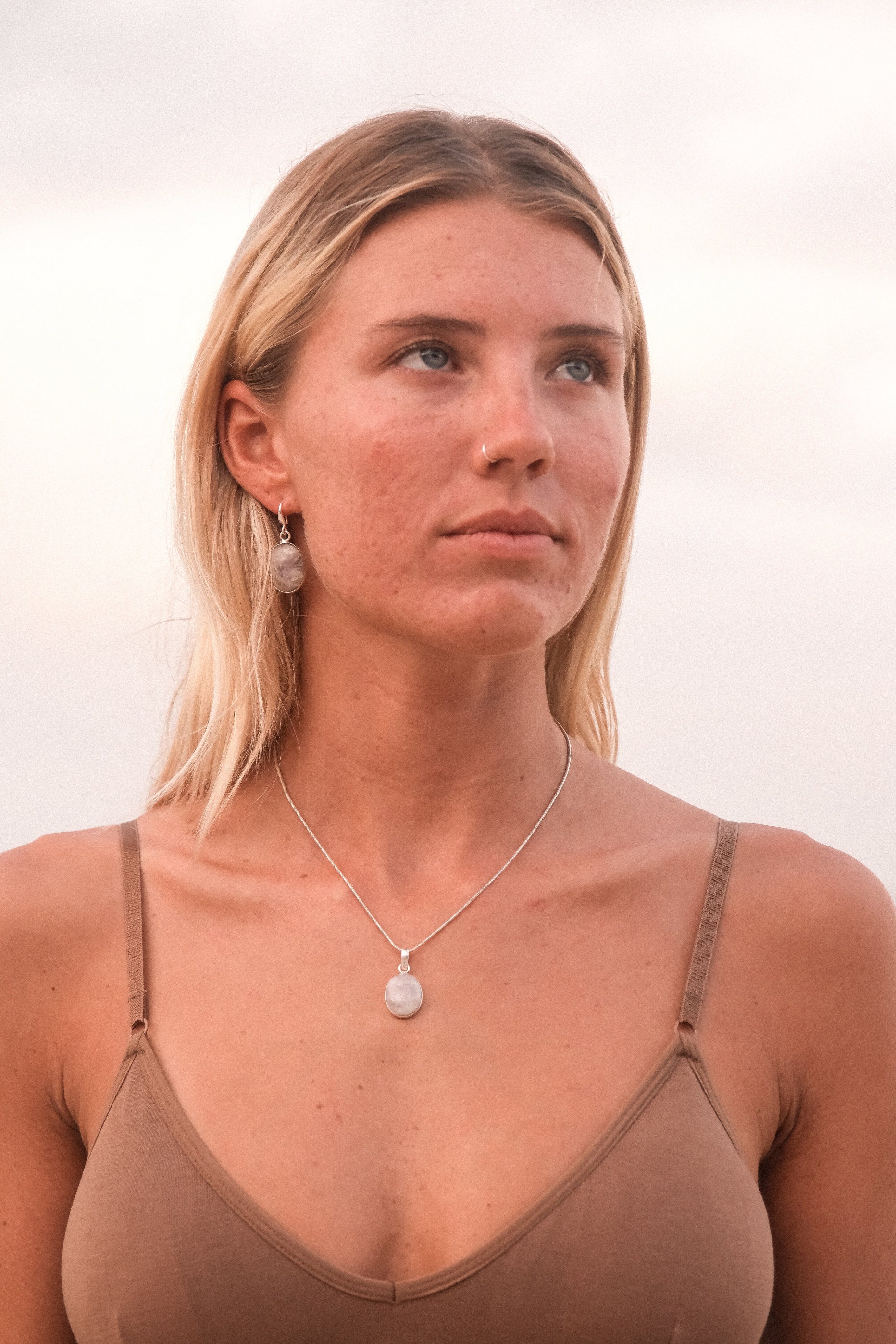 A person wearing a brown tank top and a silver pendant necklace with a moonstone.