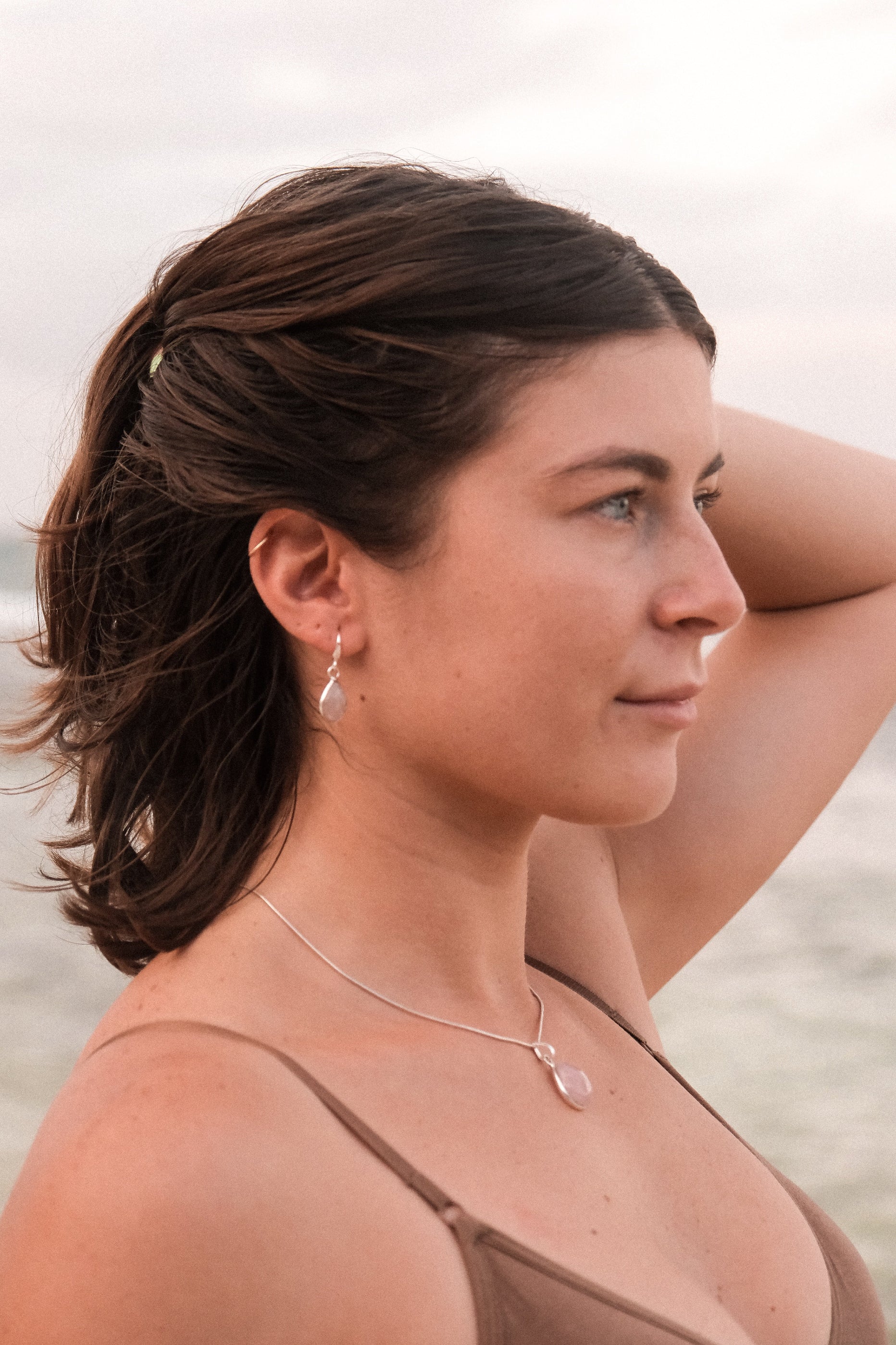 This image features a close-up view of a woman wearing elegant earrings. The earrings are designed with a simple yet captivating aesthetic, featuring a small, possibly pearl-like element attached to a delicate chain that drapes gracefully.