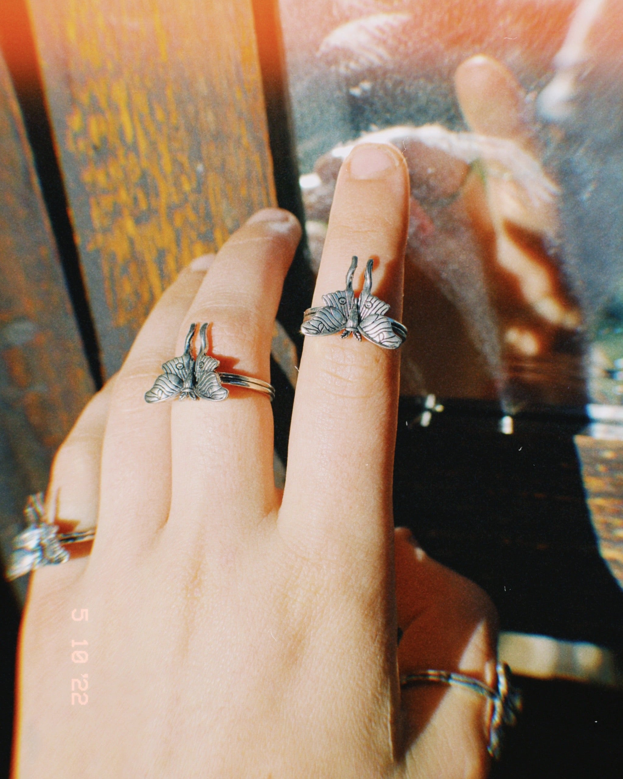 Hand wearing two silver butterfly rings with a blurred background