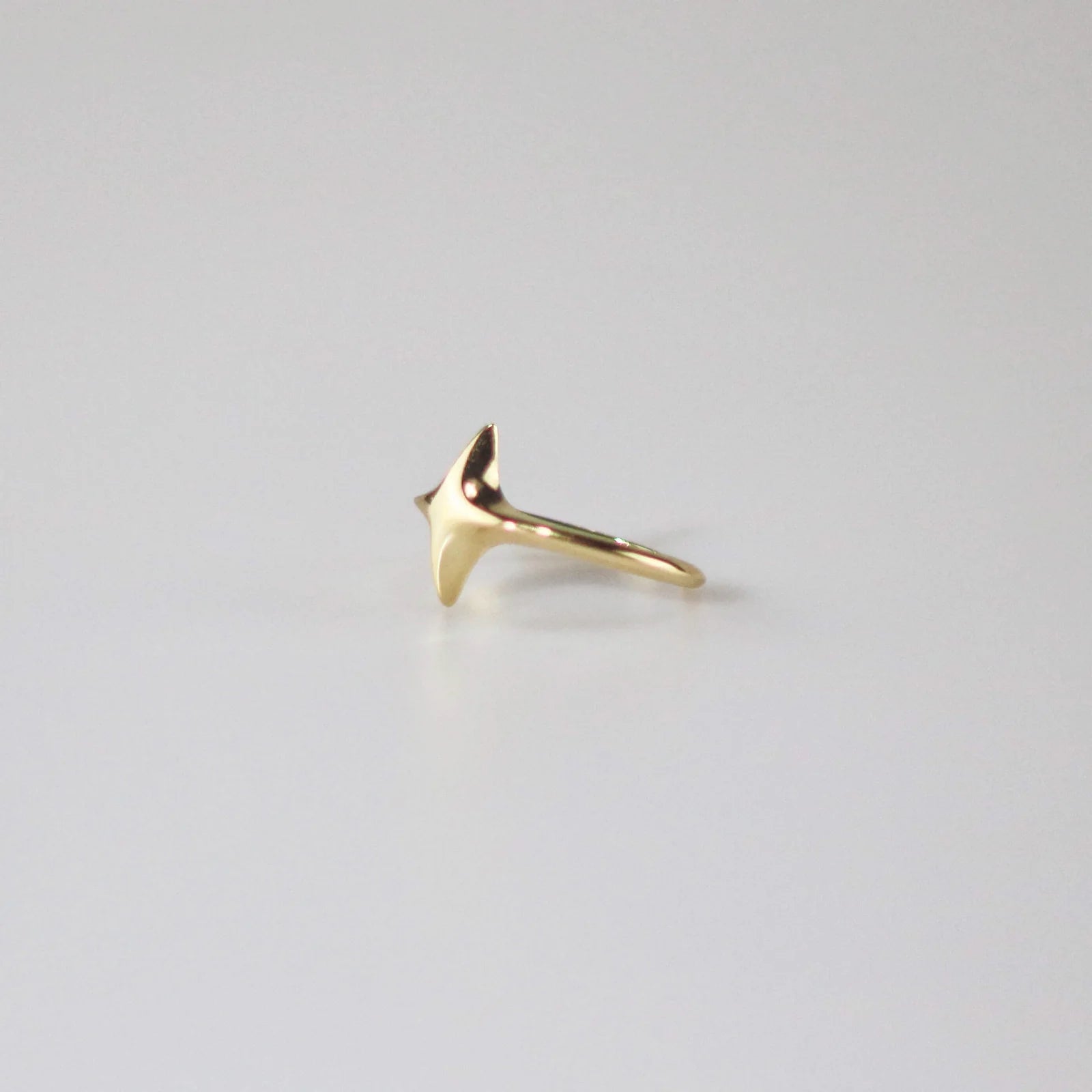 side shot of a gold-colored star-shaped ring on a white background.