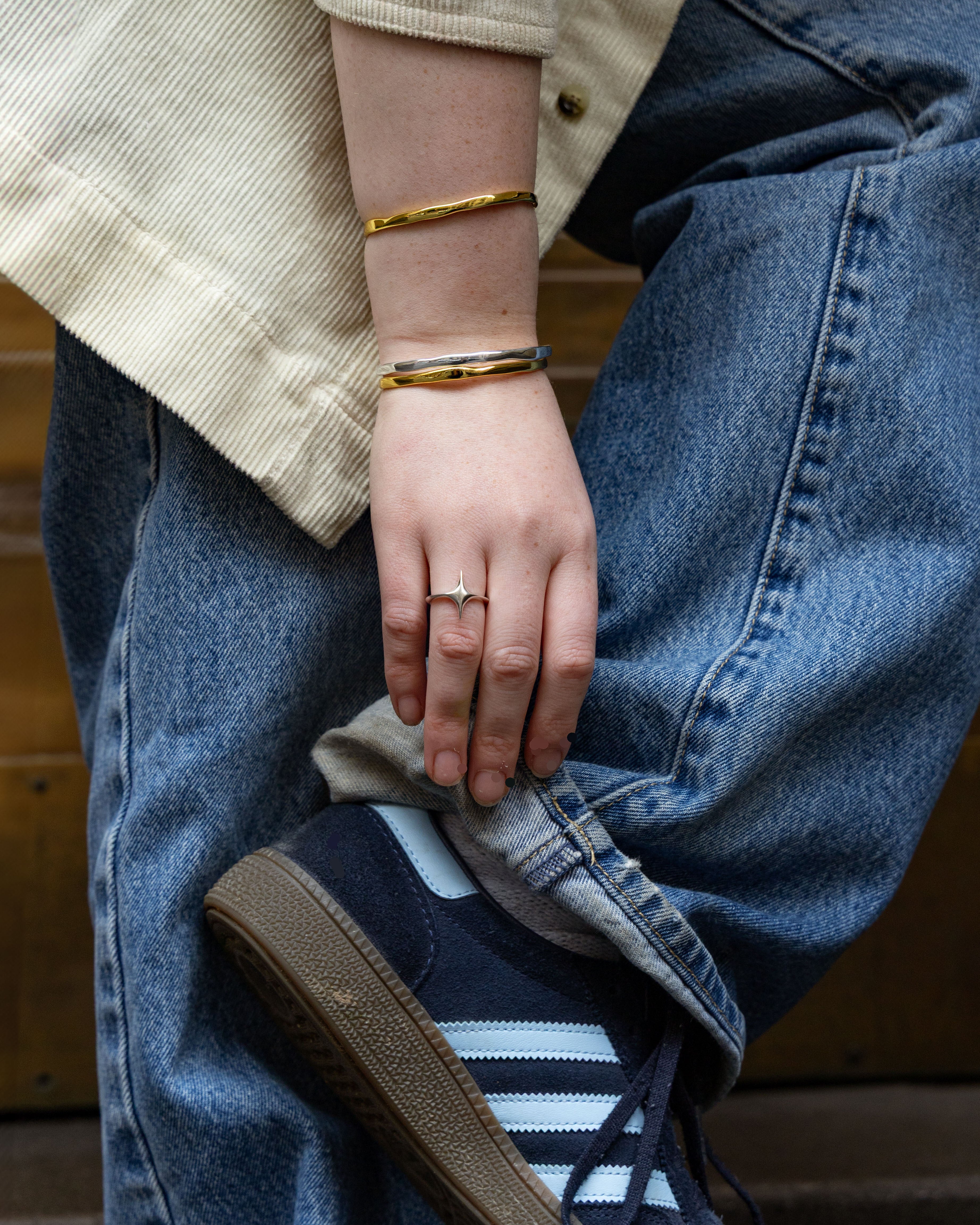 Person wearing jewellery stack, adjusting shoe 