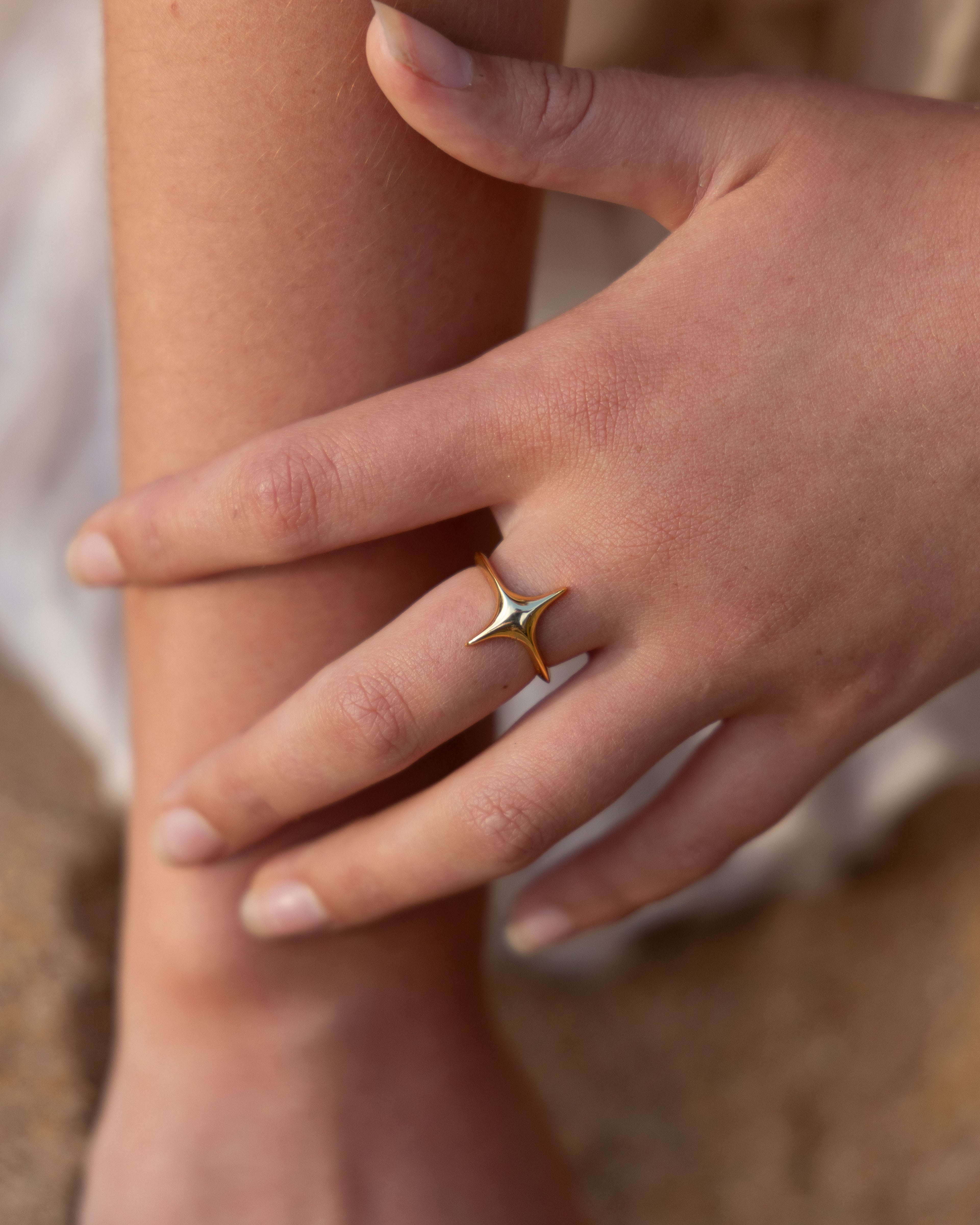 Hand wearing a gold ring with a star design on a blurred background