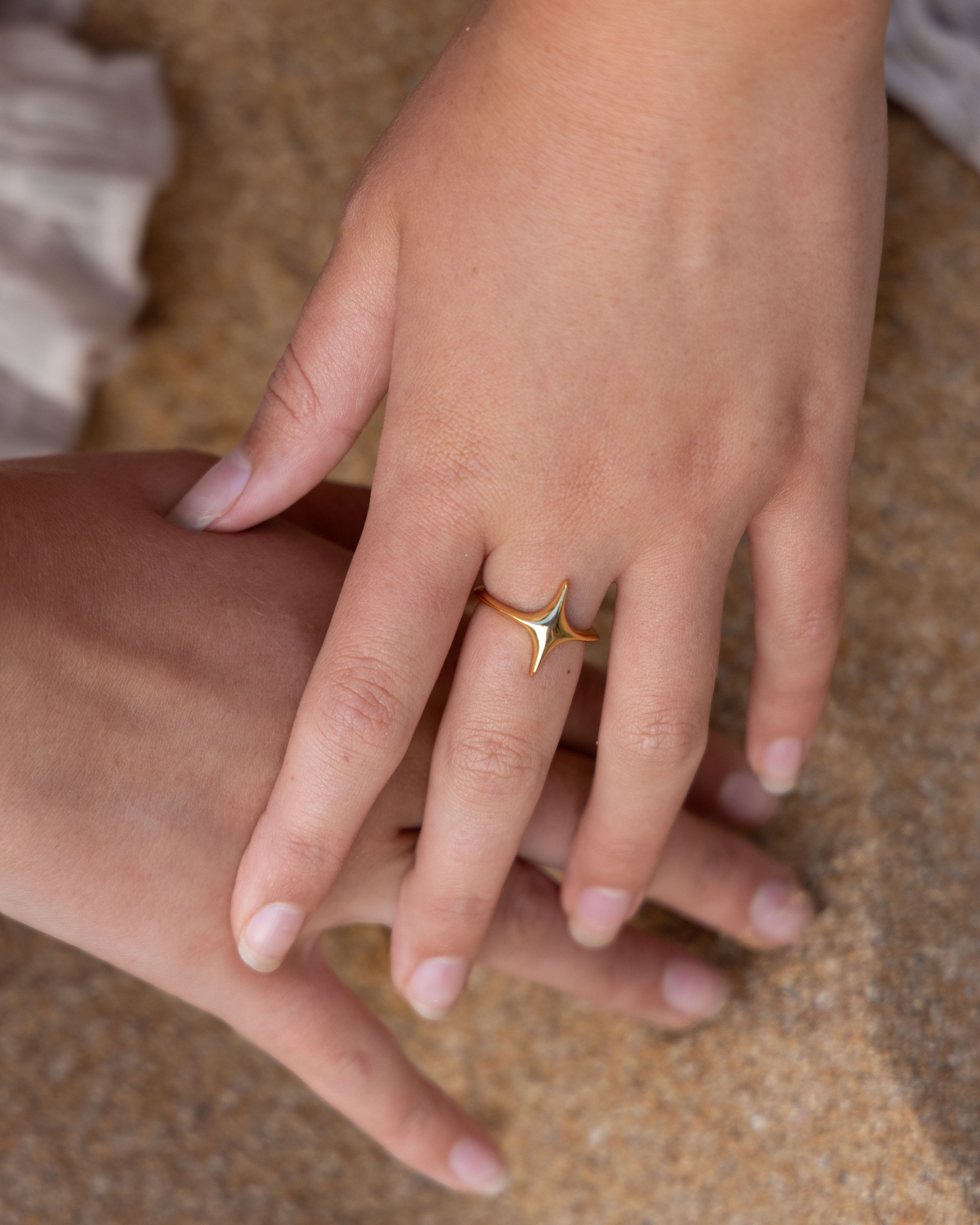 Close-up of a hand wearing a gold ring on a textured surface