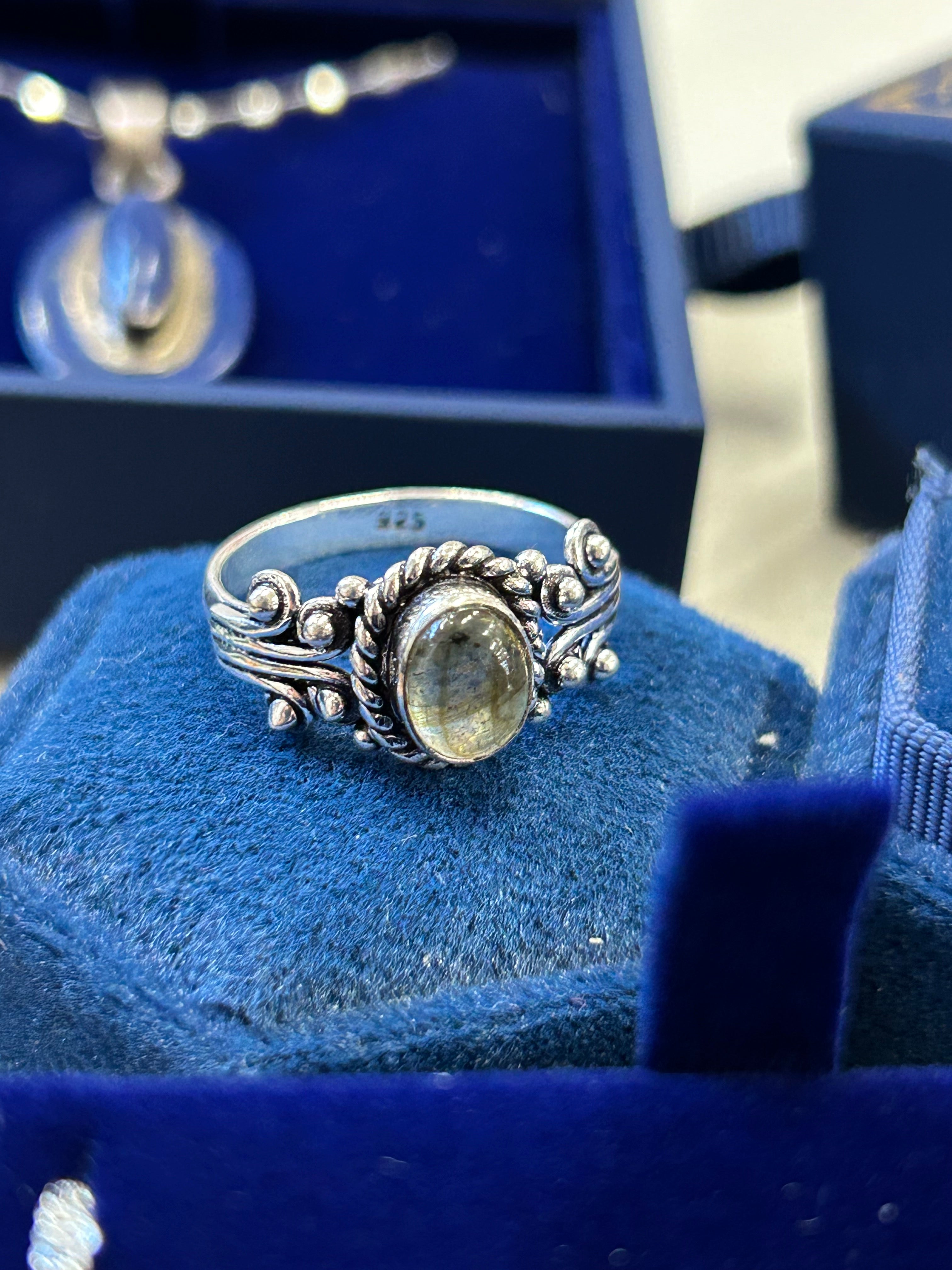 A silver ring with a labradorite stone, featuring intricate detailing 