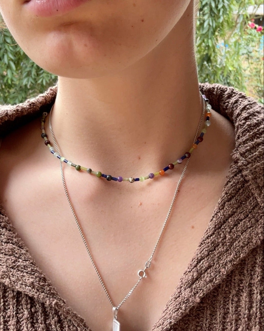 Close-up of a person wearing a crystal beaded necklace, outdoors.