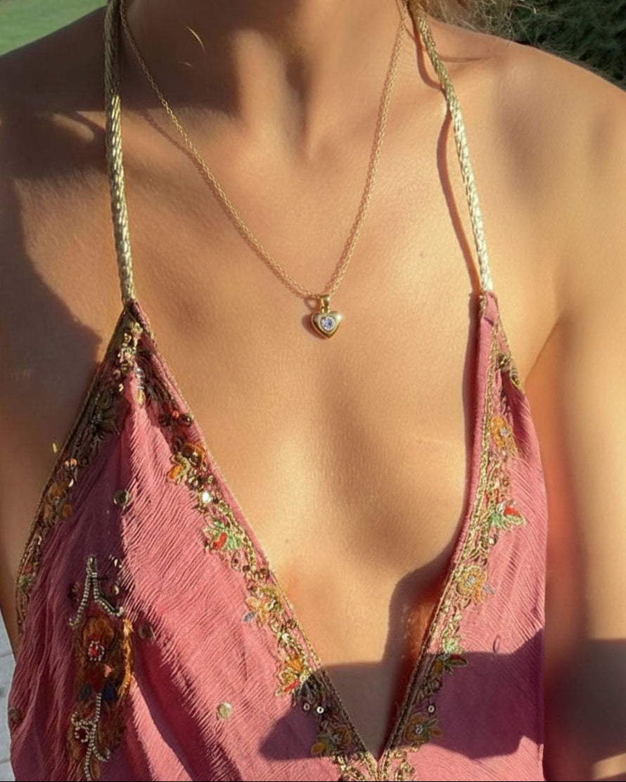 Close-up of a pink dress with floral patterns and a gold necklace with a heart pendant.