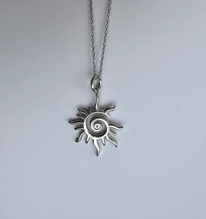 Silver sun-shaped pendant necklace on a light gray background